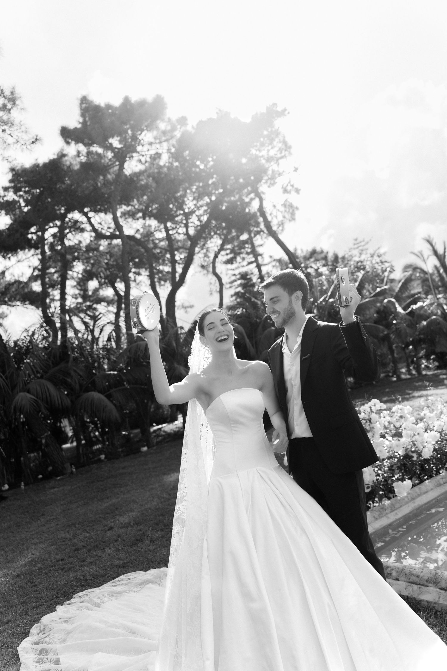 Black and white photo of a joyful bride in a strapless gown and groom in a suit celebrating outdoors.