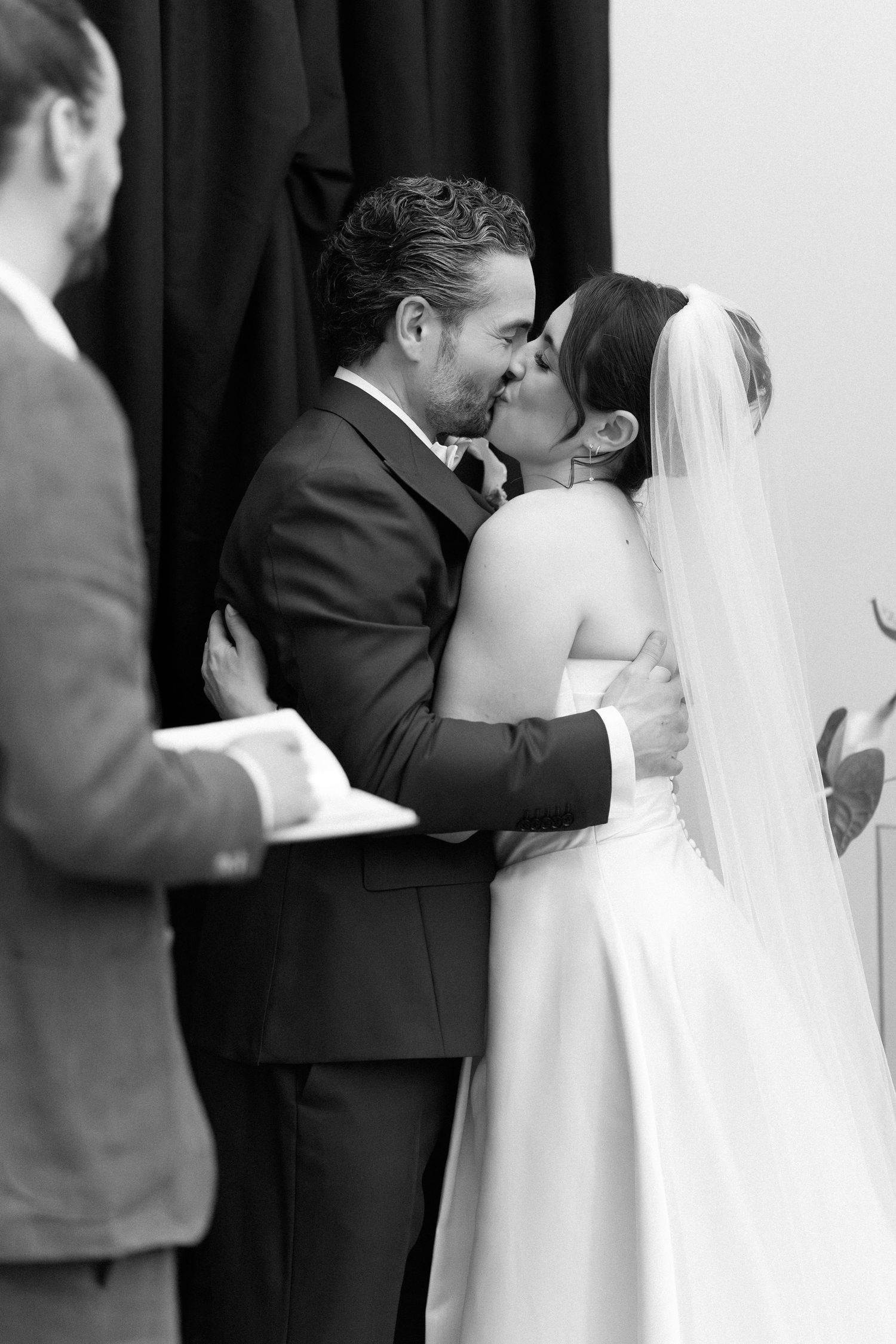 Black and white photo of a bride and groom sharing their first kiss at the wedding ceremony.