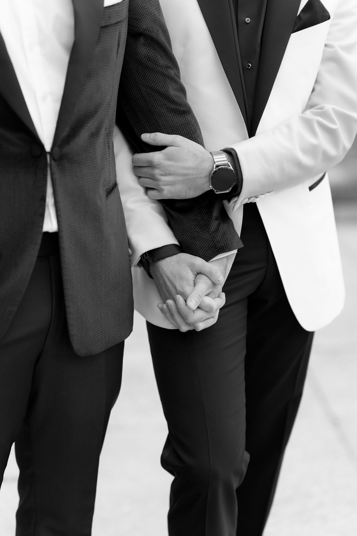 Black and white photo showing two people holding hands while wearing contrasting black and white formal suits.