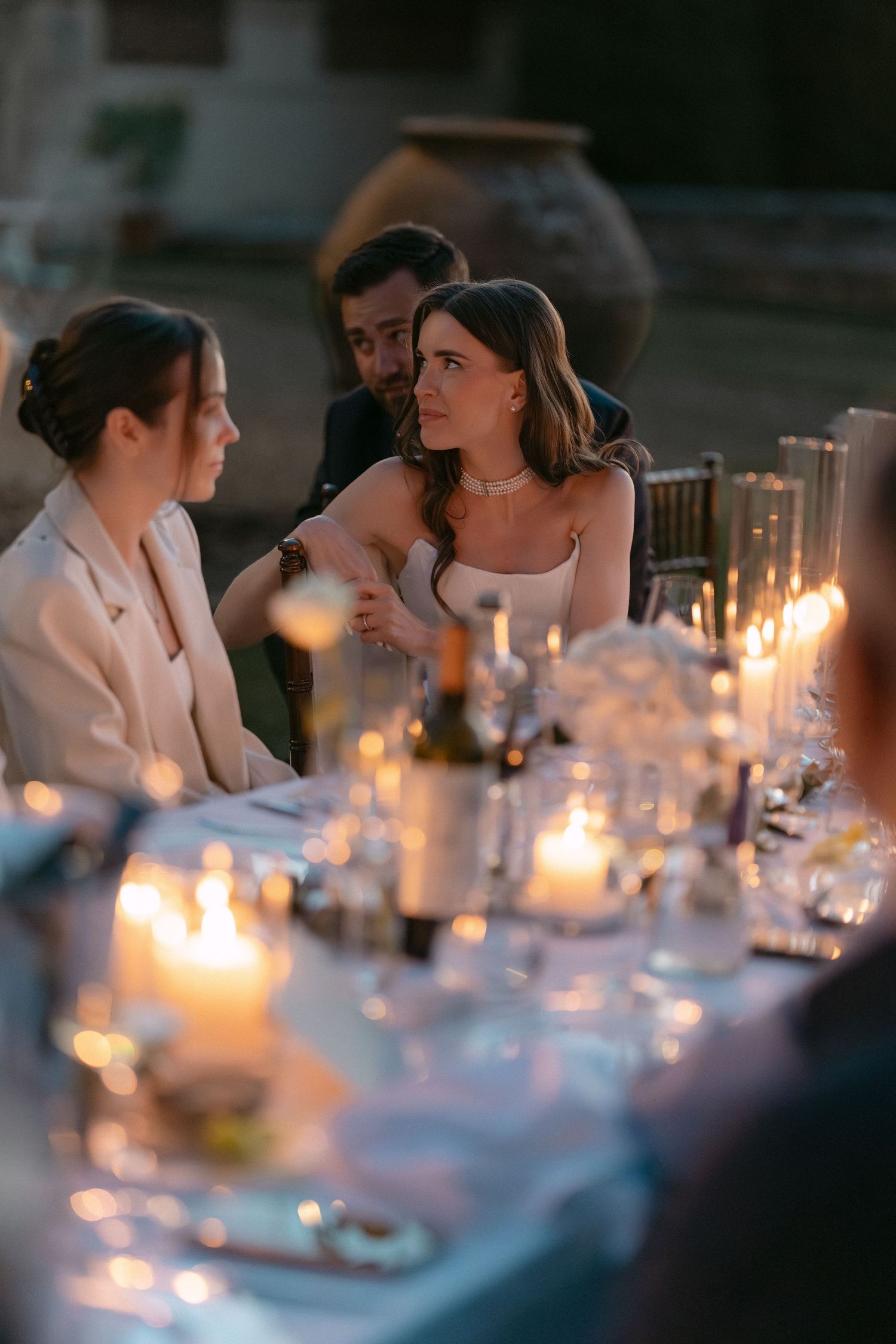 Bride and groom share an intimate moment at candlelit wedding reception dinner table with glowing candles.