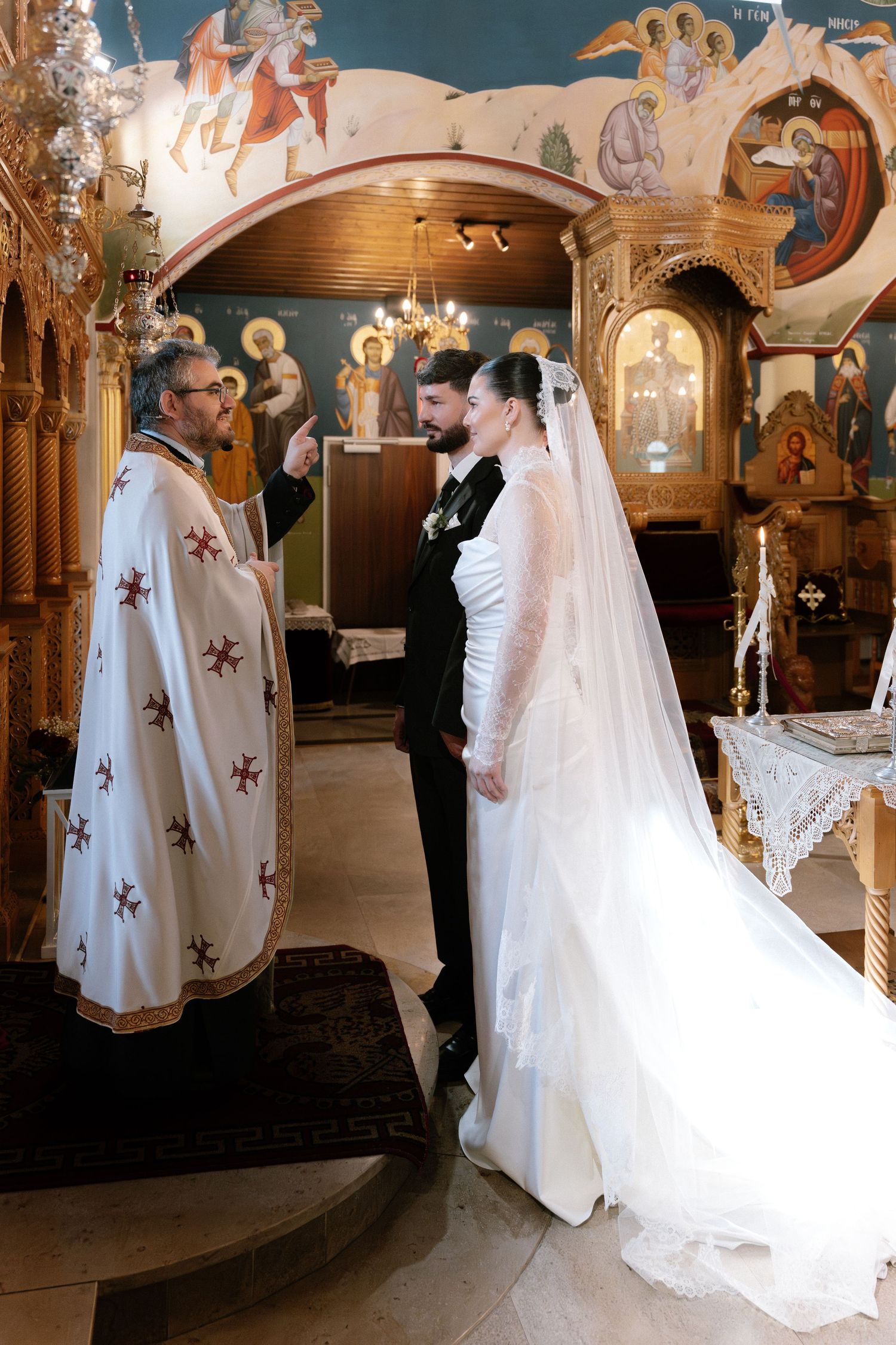 Orthodox wedding ceremony with priest blessing bride and groom in ornate church with Byzantine icons.
