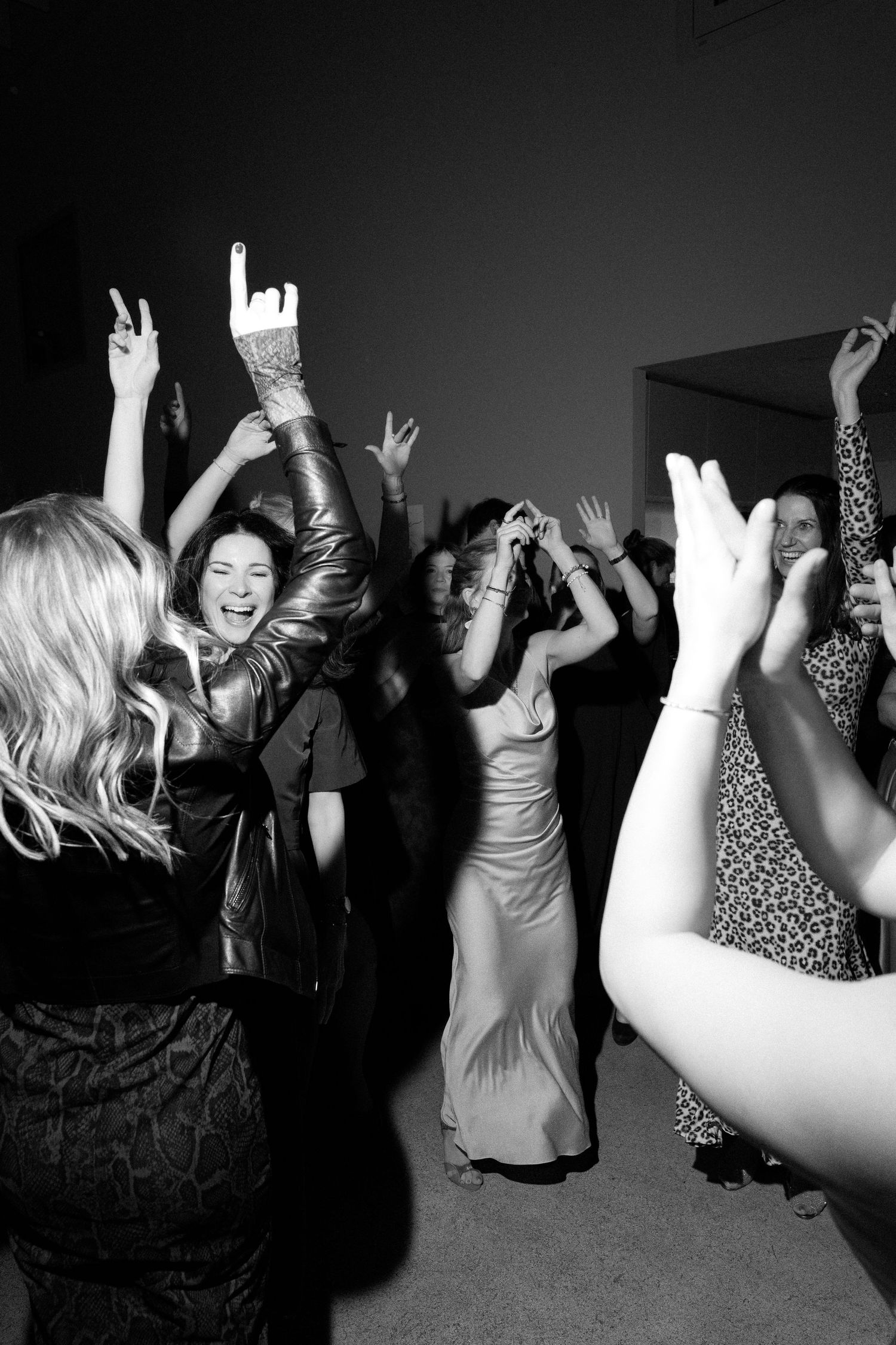 Black and white photo of joyful guests dancing at a lively party, raising hands and smiling on the dance floor.