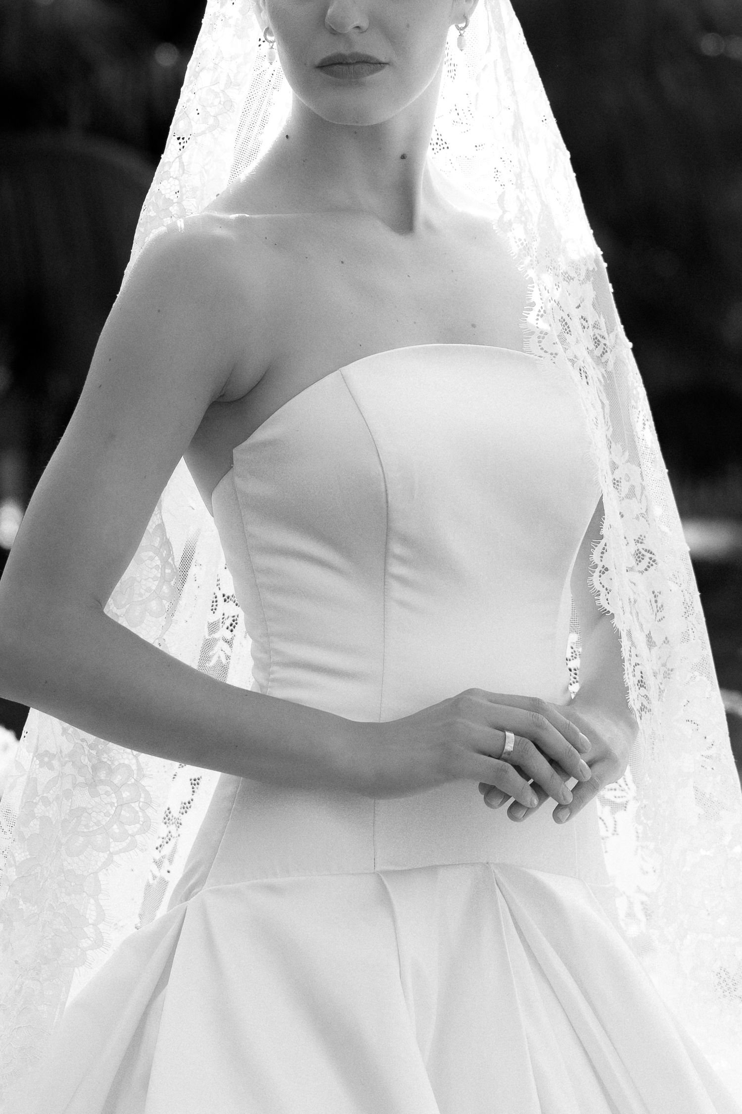 Black and white photo of a bride in a strapless wedding gown with lace veil and diamond ring.