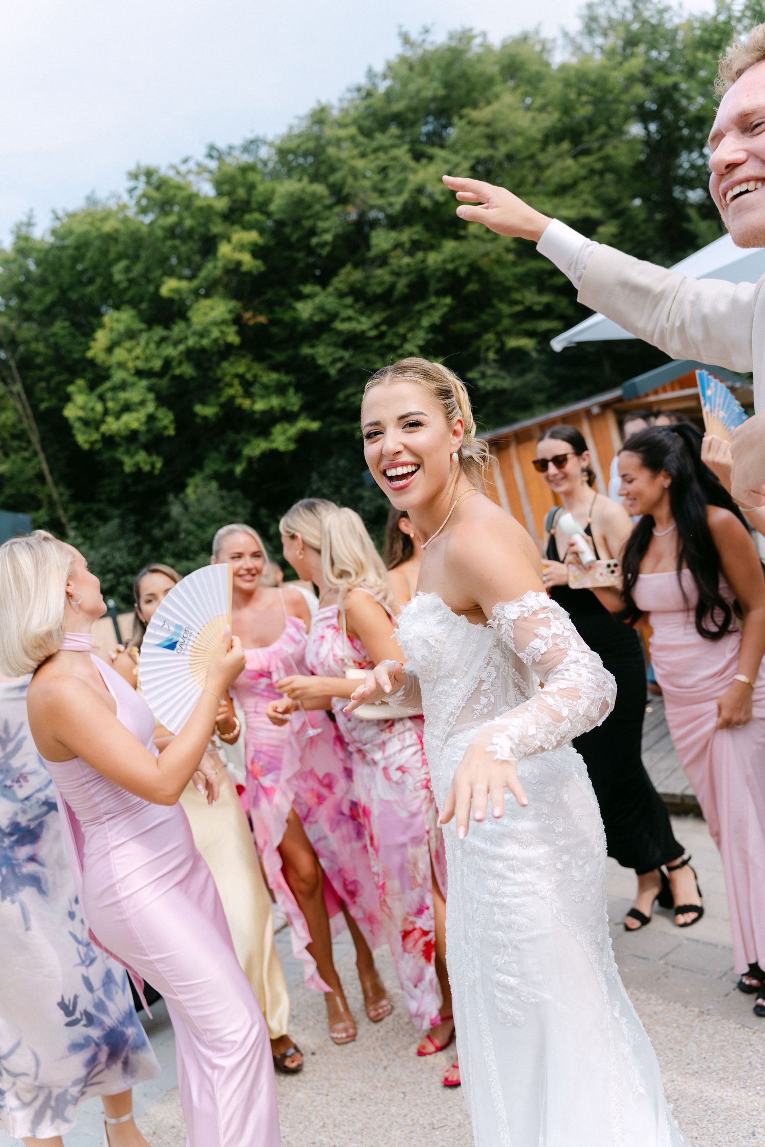 Wedding party dancing and celebrating outdoors in pink dresses and white gown during a summer celebration.