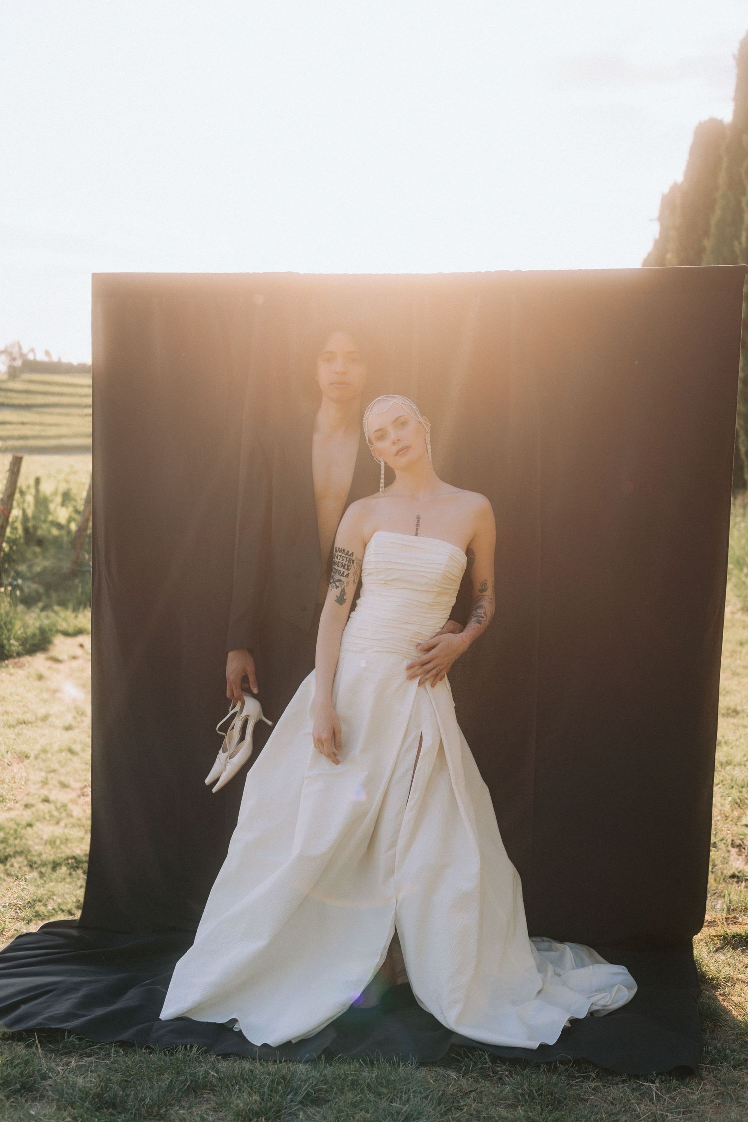 A bride in a flowing white wedding dress poses against a dark backdrop during a golden hour photoshoot.