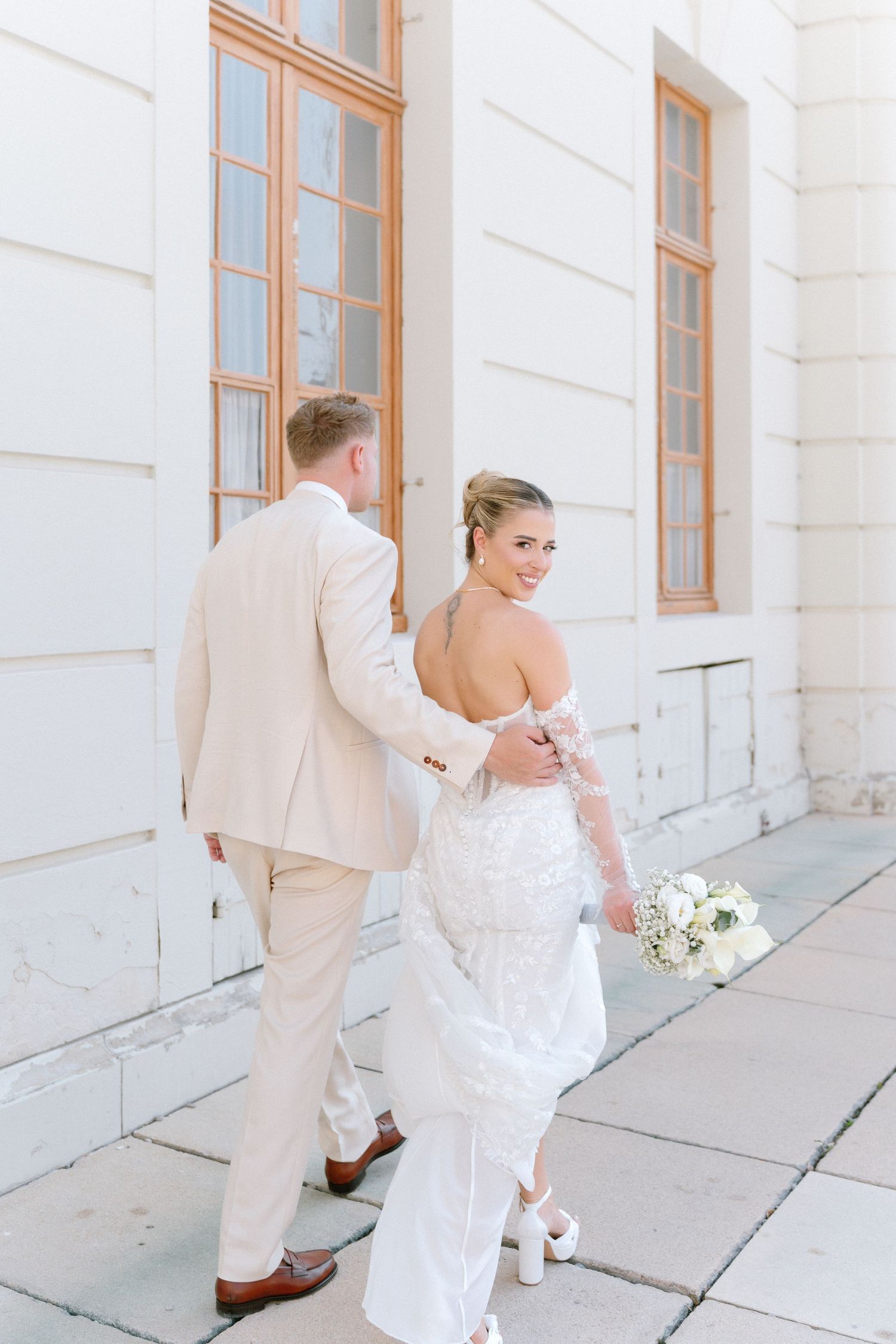 Wedding couple walking along white building exterior with copper-colored window frames in a romantic sequence. Schloss Ludwigsburg