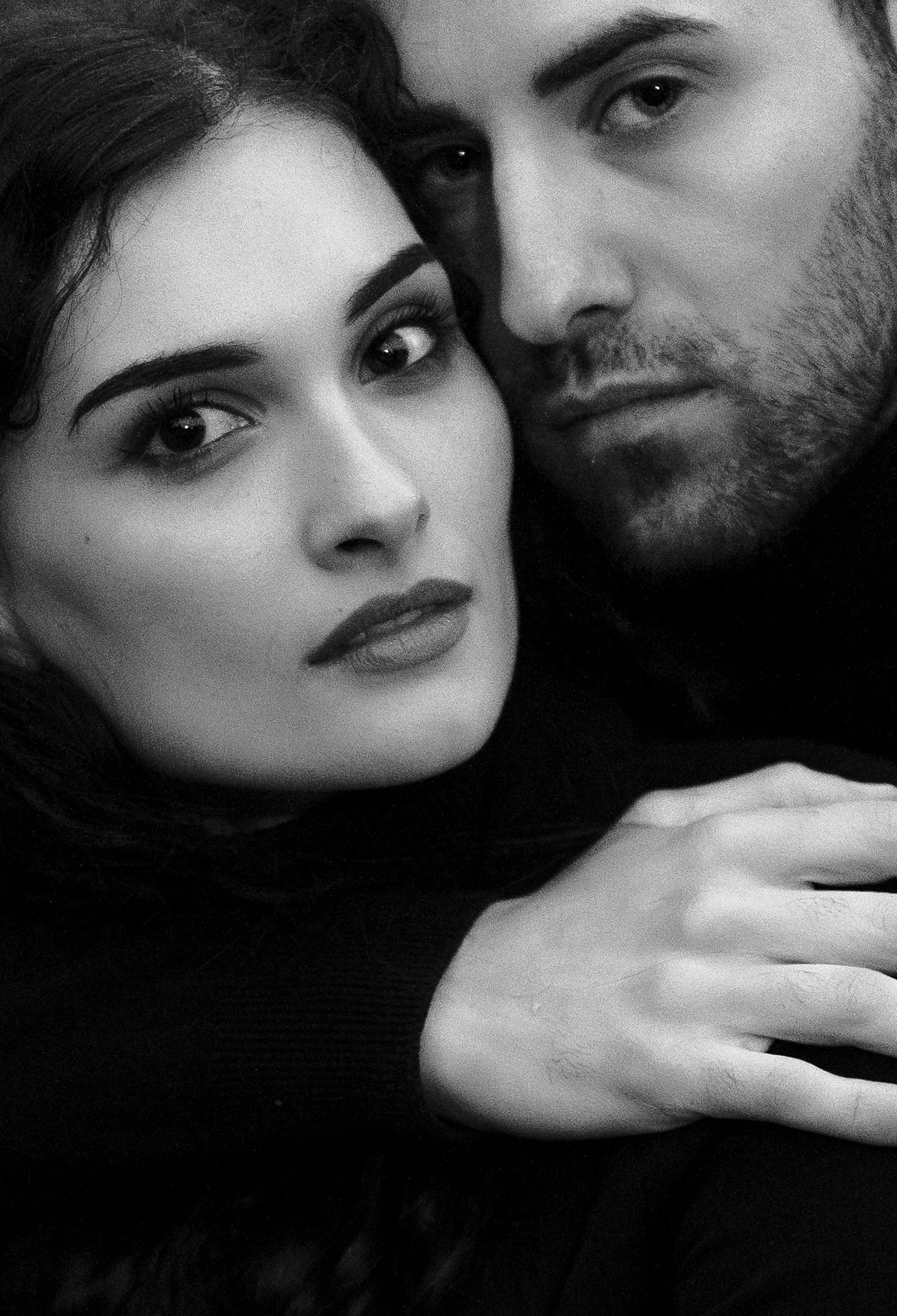 Dramatic black and white close-up portrait of a couple in an intimate pose against dark background.