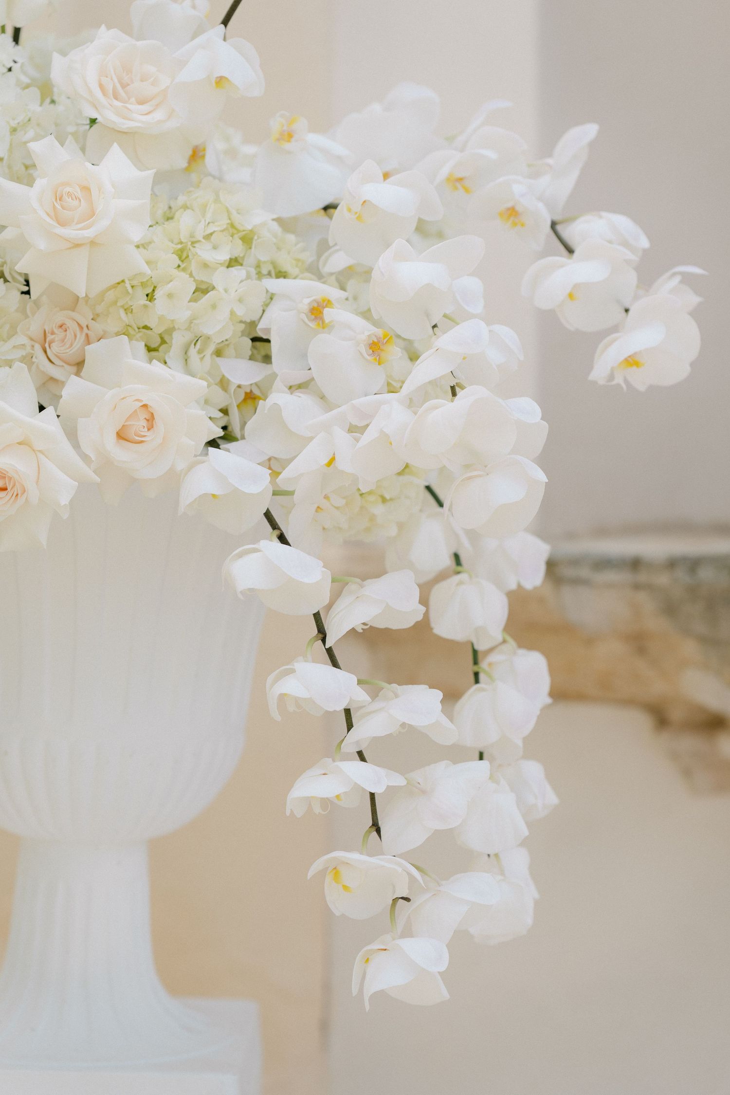 Elegant white floral arrangement featuring cascading orchids and roses in a white vase.