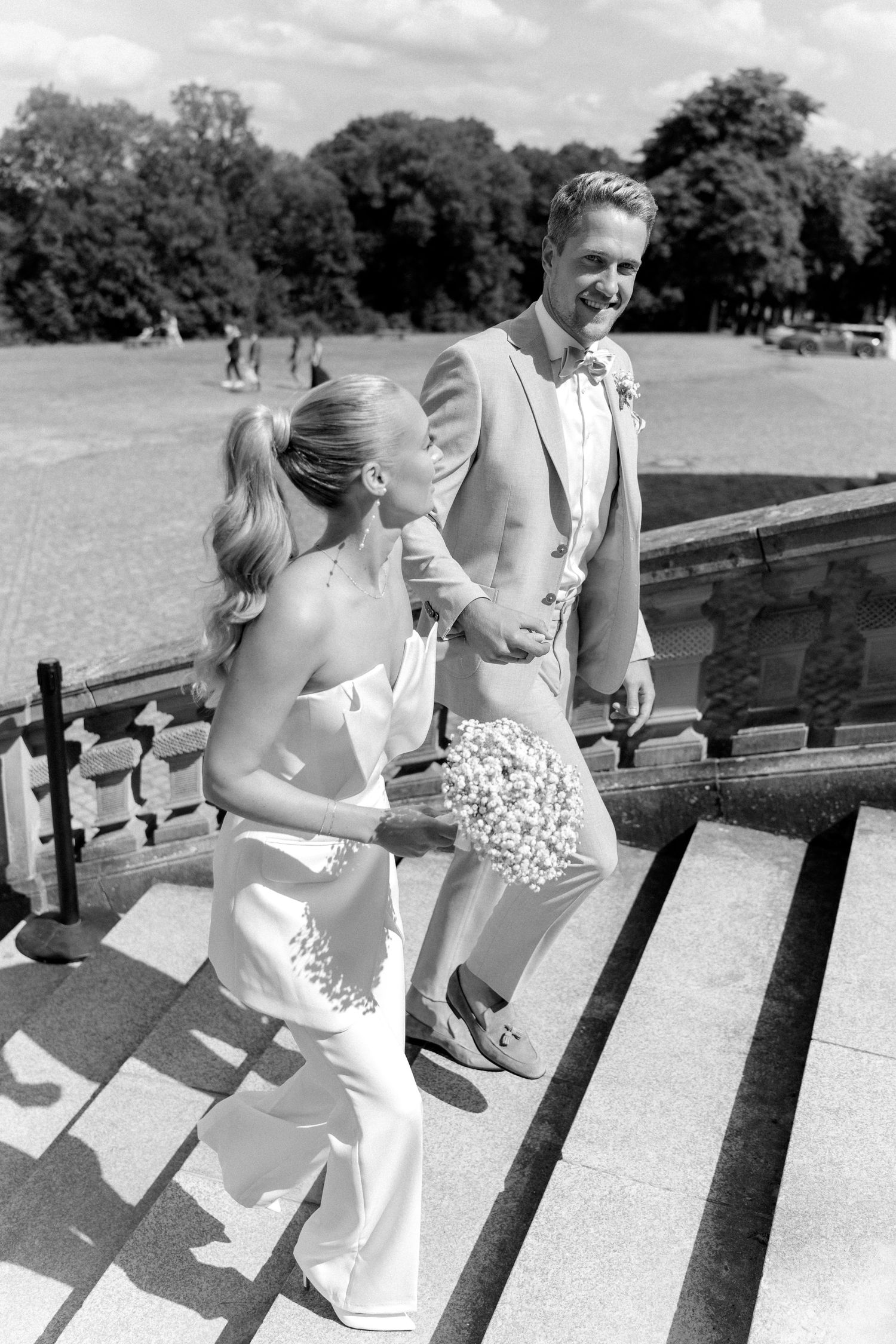 Black and white vintage photo of people lounging on a wooden bench in summer attire at a park. Schloss Solitude