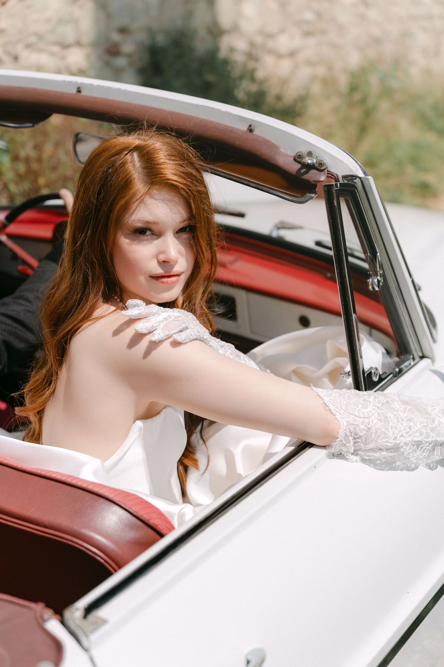 A vintage white convertible car with red leather interior shown from the passenger side on a sunny day.
