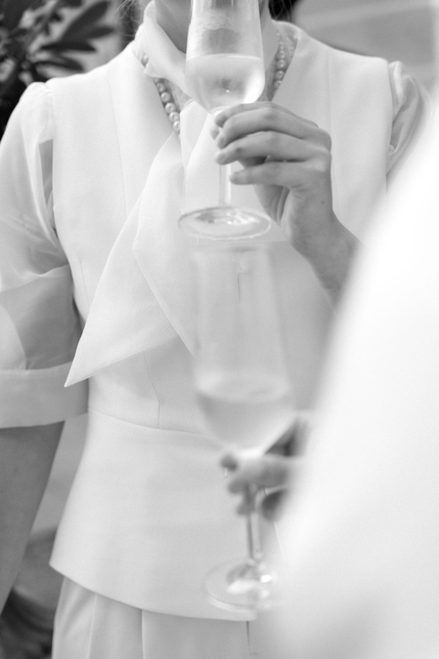 Black and white photo of a woman in white suit holding a champagne glass at a formal event.