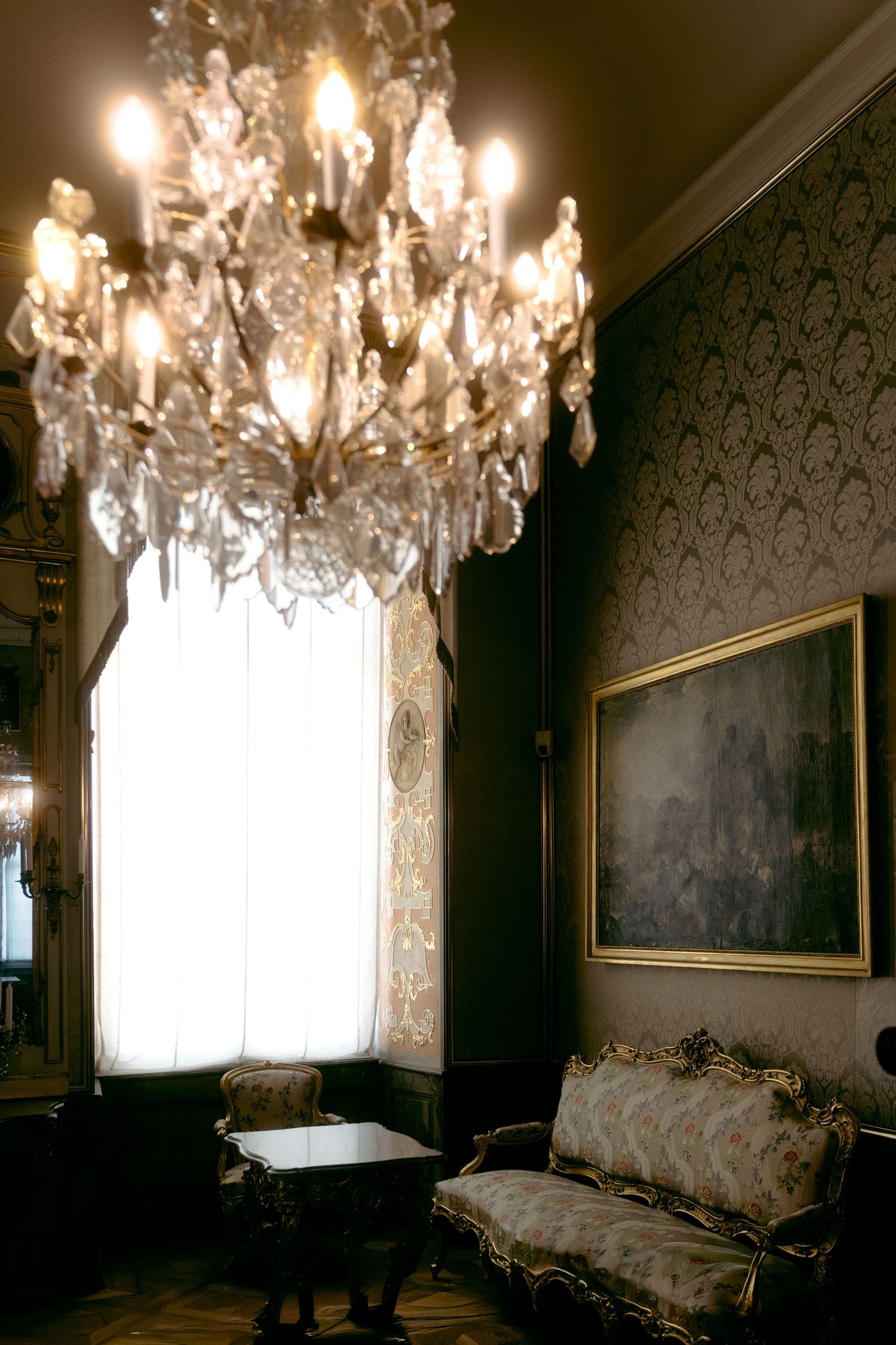 Elegant crystal chandelier illuminates a dark Victorian-style room with ornate wallpaper and antique furnishings. Schloss Ludwigsburg