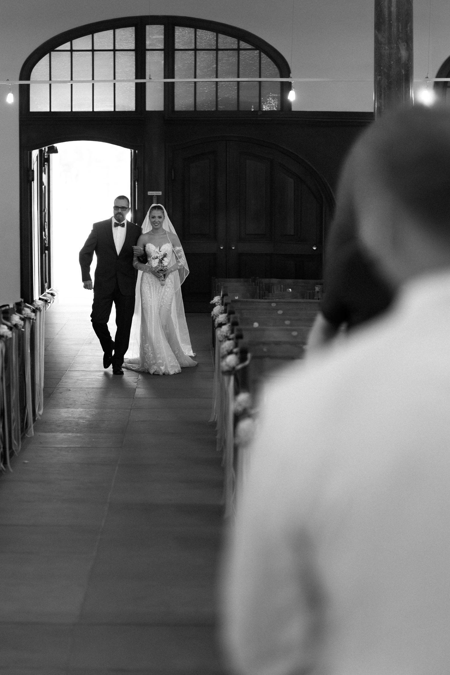 A black and white sequence of wedding ceremony photos showing the procession walking down a hallway with arched windows.
