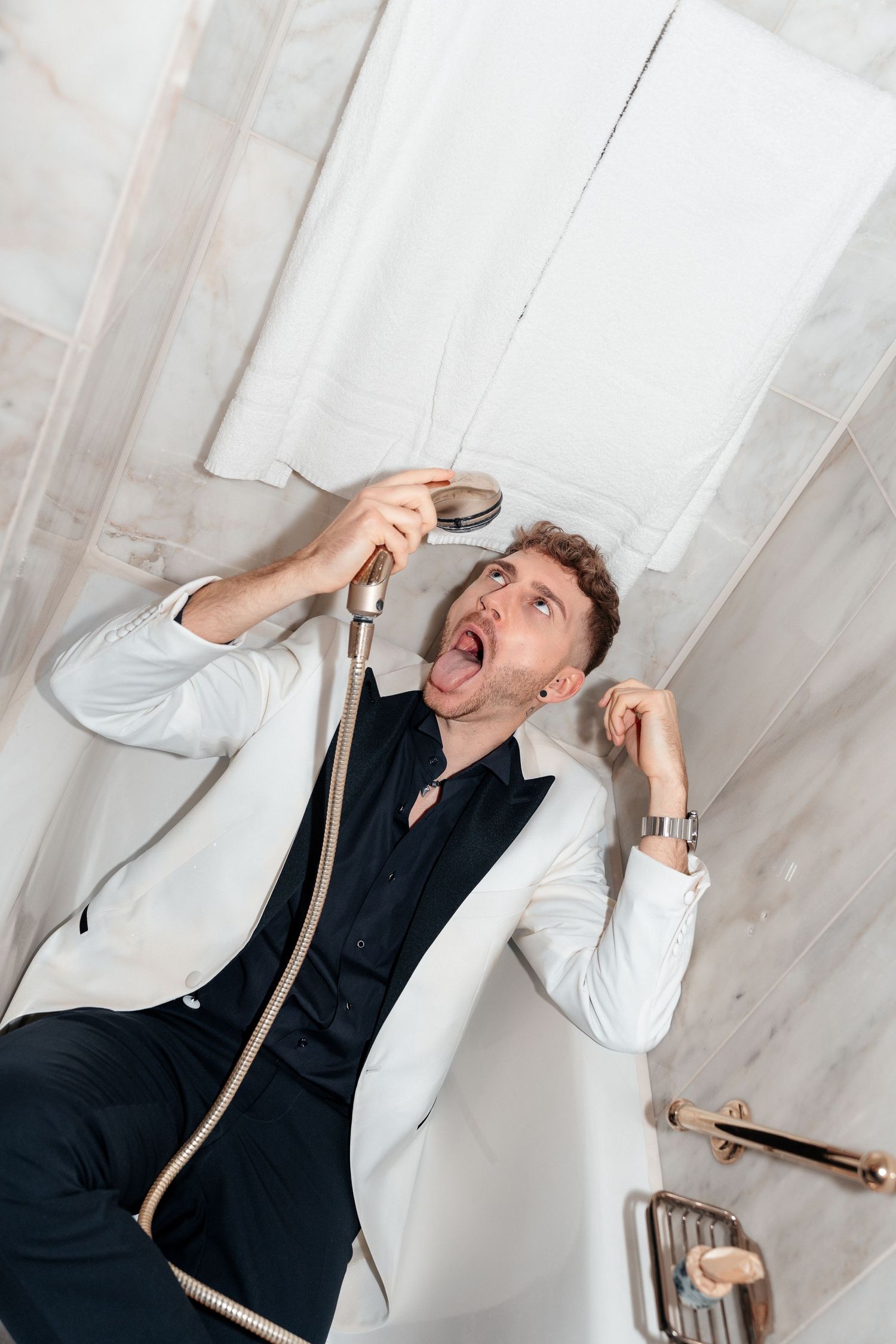 Energetic performer in white blazer and black shirt sings passionately into a microphone against white background.