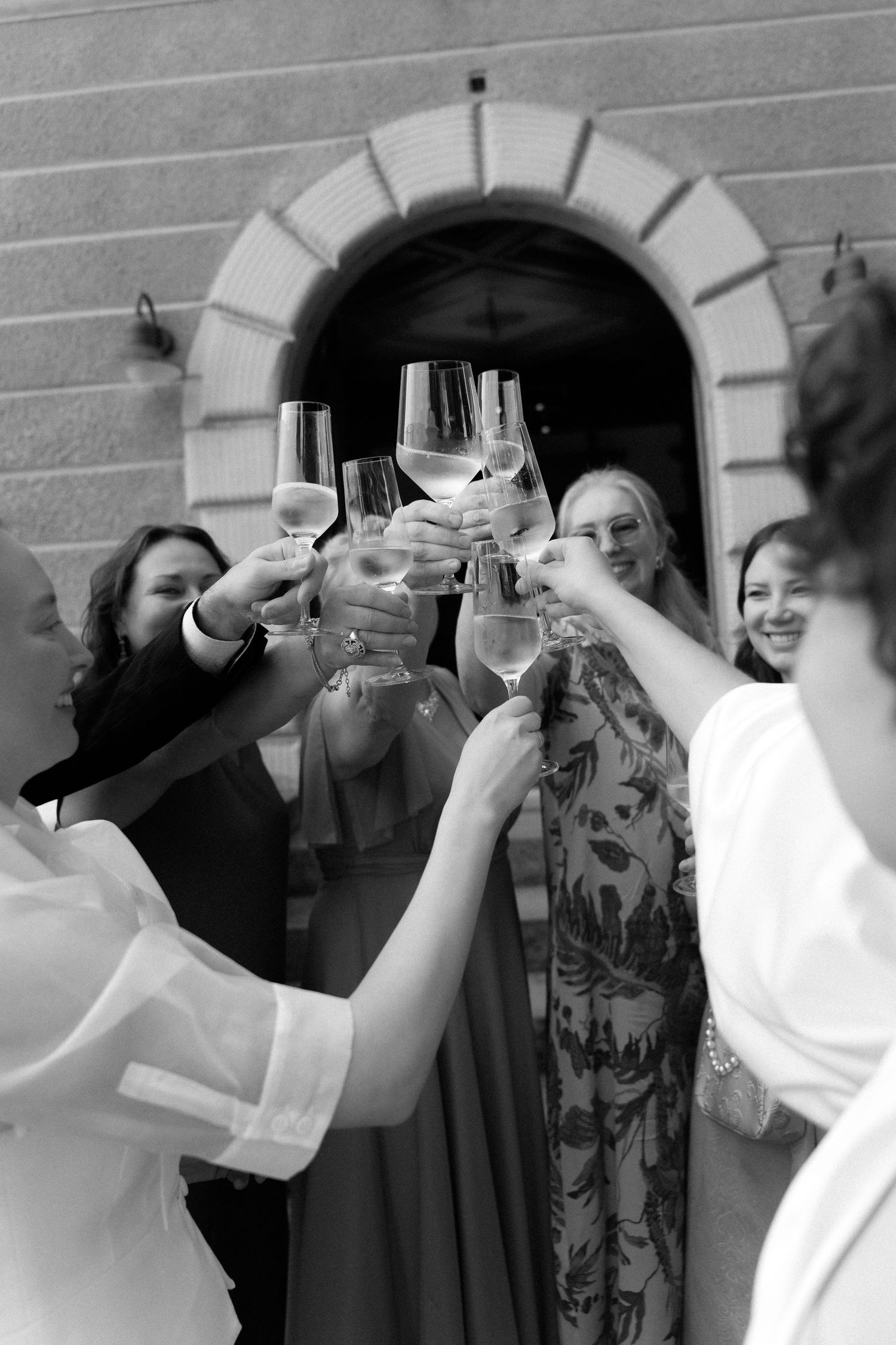 Black and white photo of a group of women toasting with wine glasses outside a stone building.