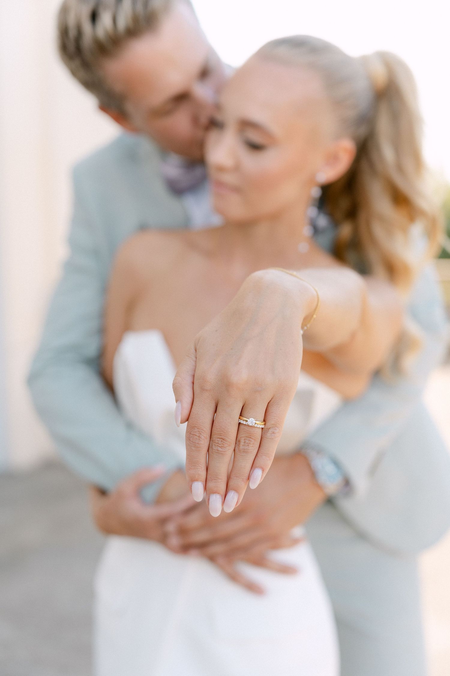Close-up of an engagement ring on bride's hand with couple embracing in soft focus background. Schloss Solitude