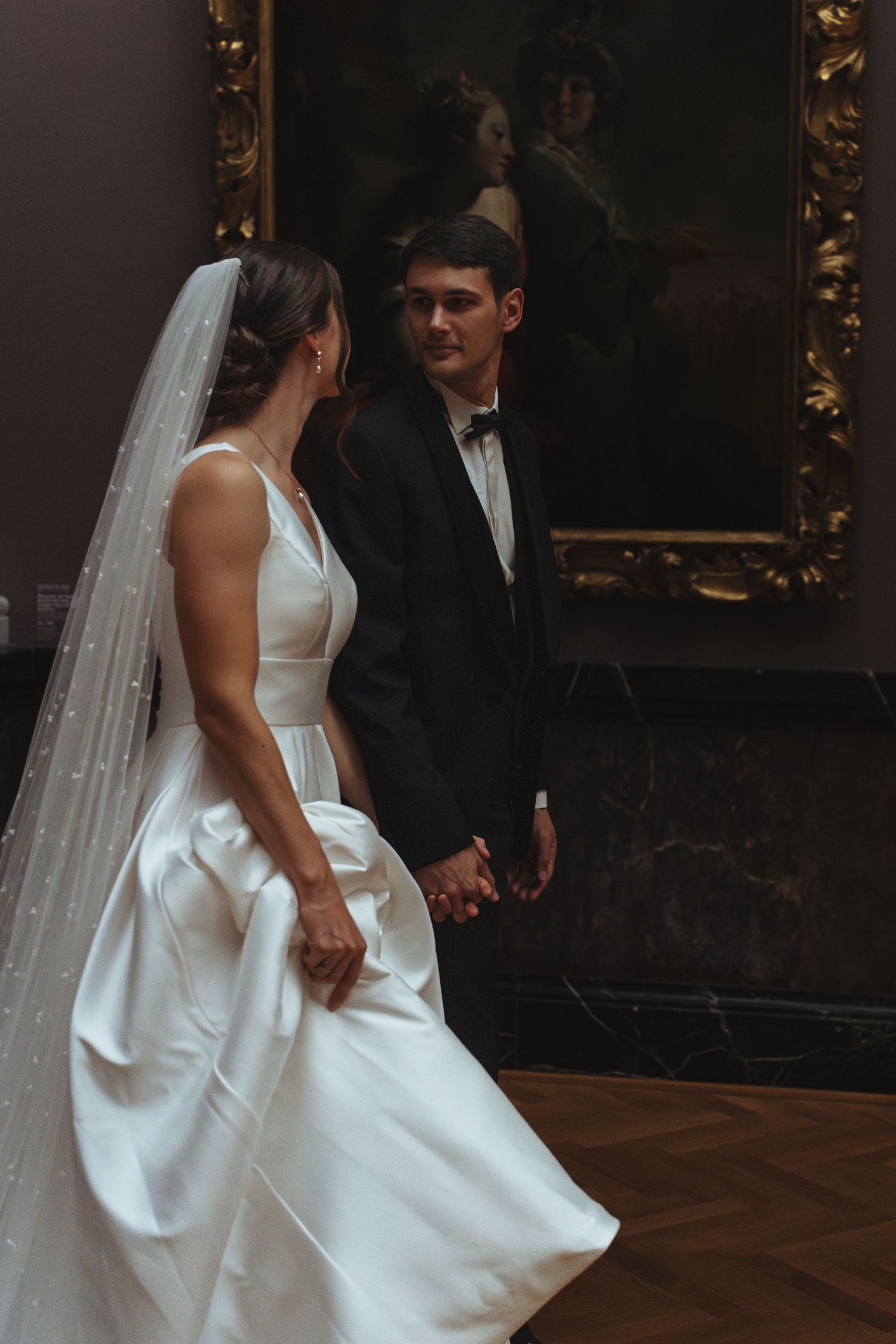 A couple shares their first dance at their wedding reception in an elegant dark-paneled ballroom.