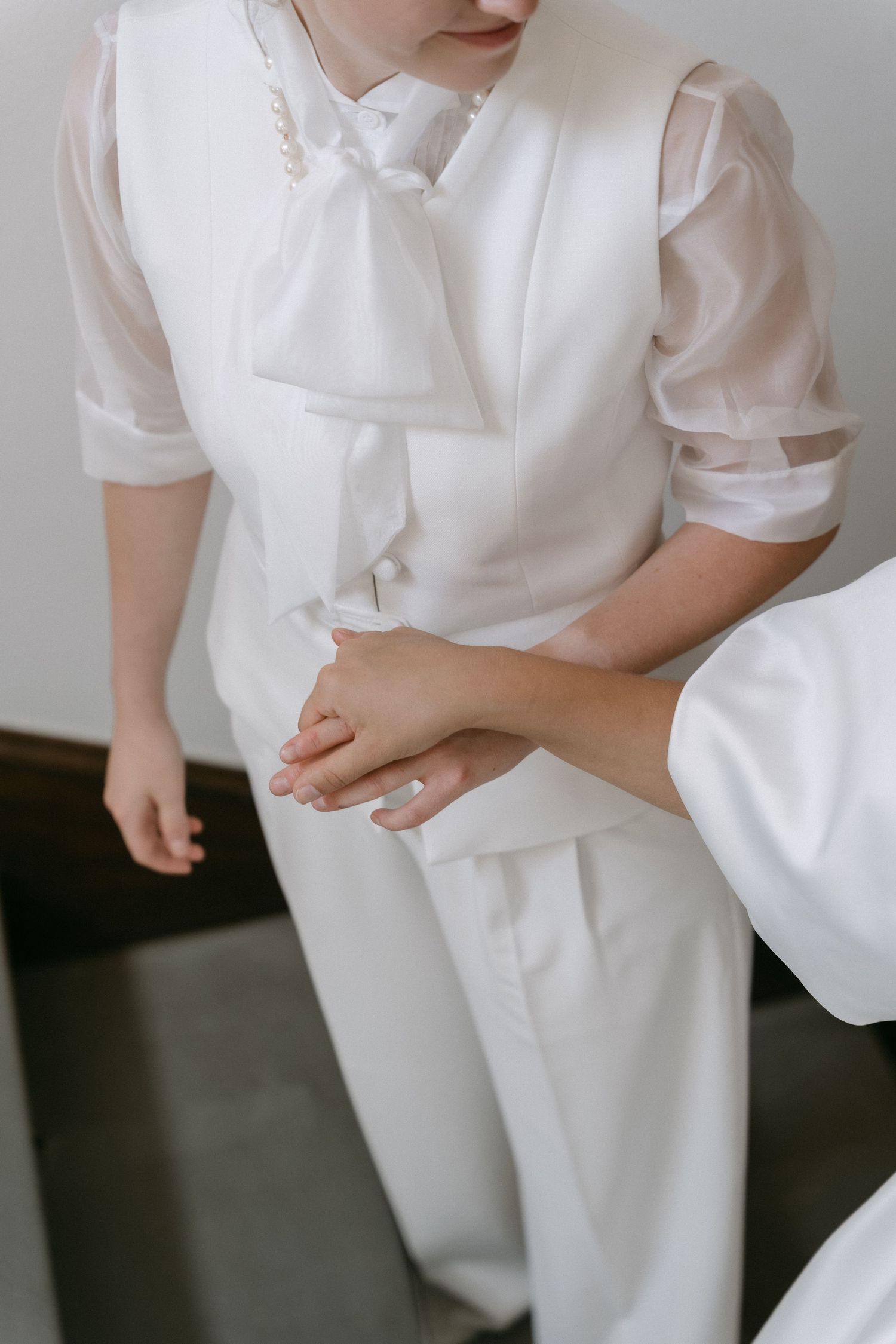 Child in white communion outfit with bow tie and vest, hands clasped together in prayer pose.