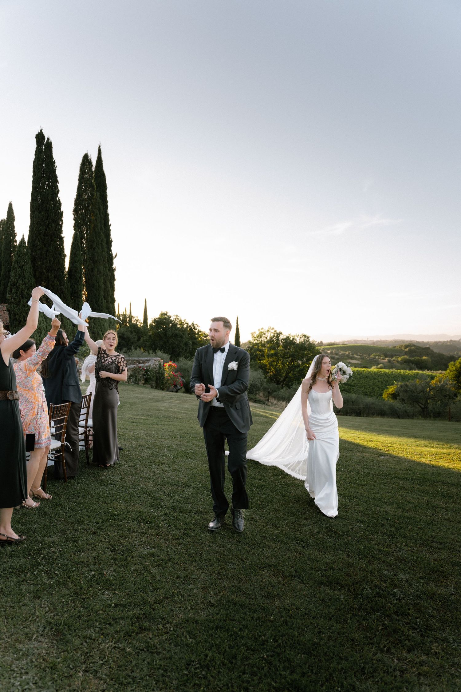 Bride and groom walk through guest sendoff line at outdoor vineyard wedding ceremony at golden hour.
