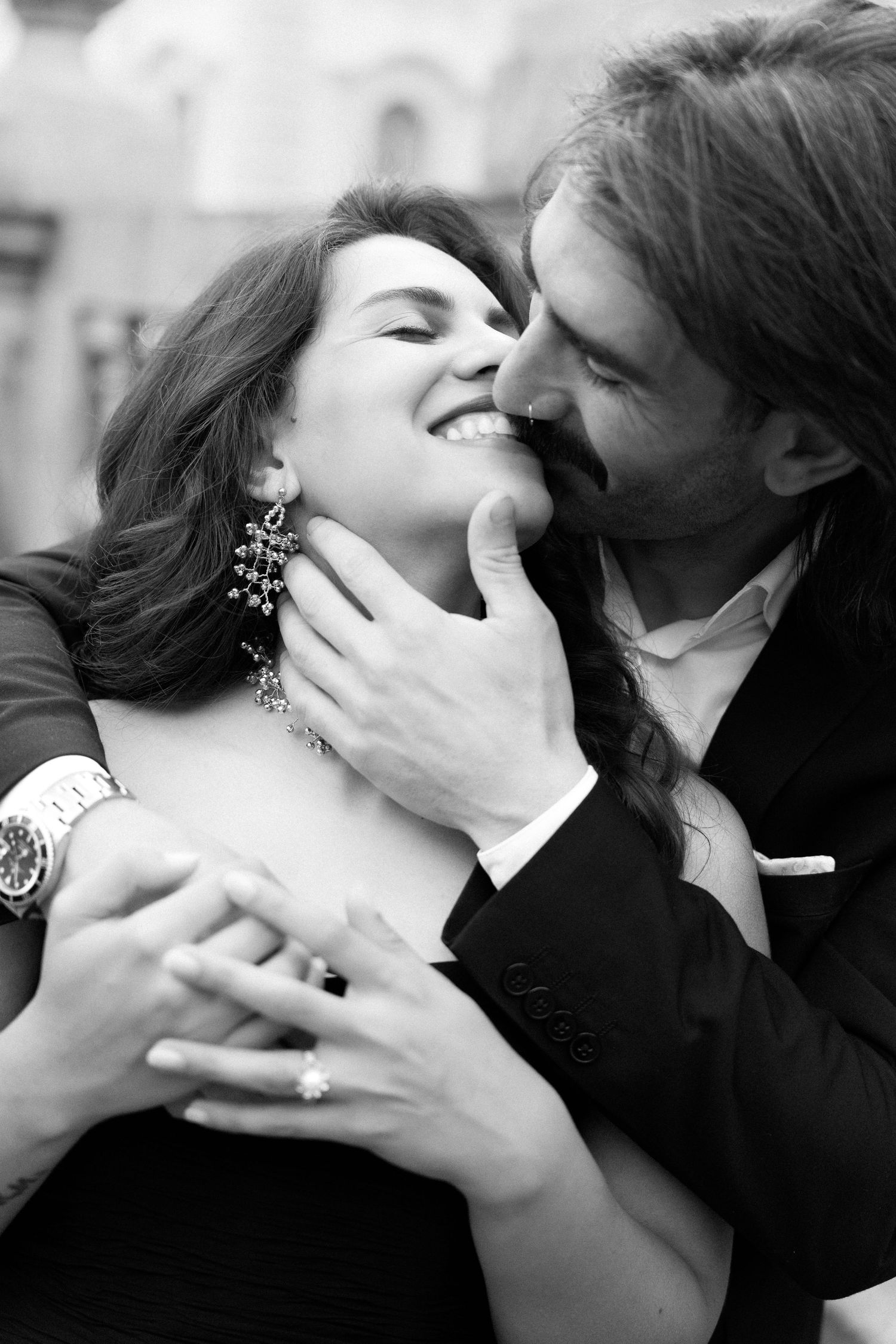 Black and white photo of a romantic couple embracing, woman smiling as man leans in to kiss her cheek.