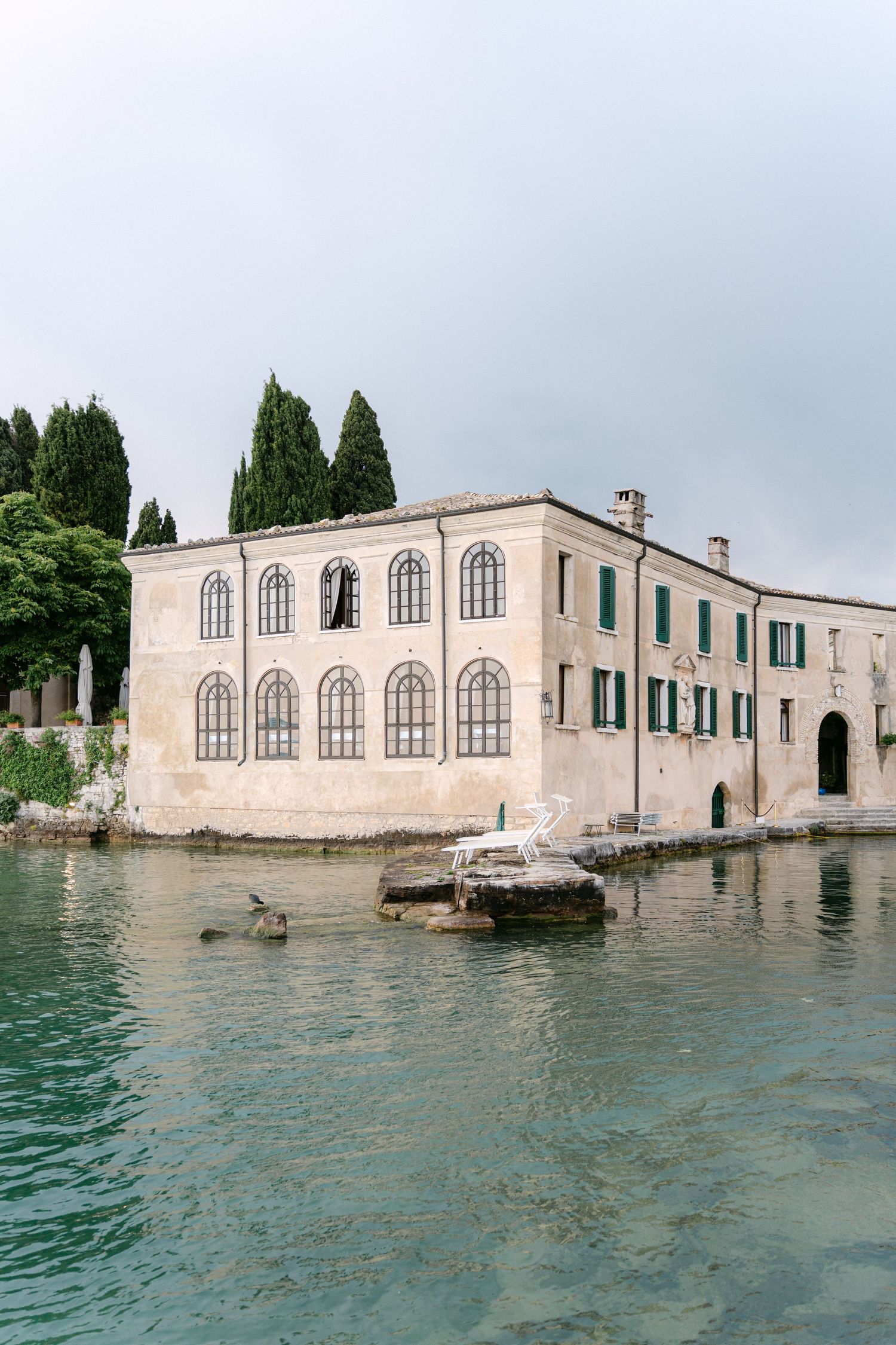 Historic waterfront building with arched windows partially submerged in turquoise waters.