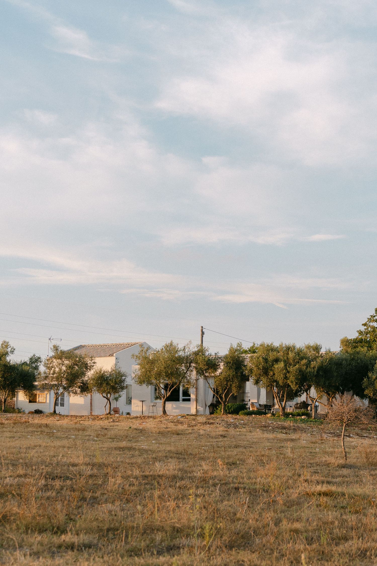 Rural landscape with white buildings scattered along a dry grassy hillside under blue sky.