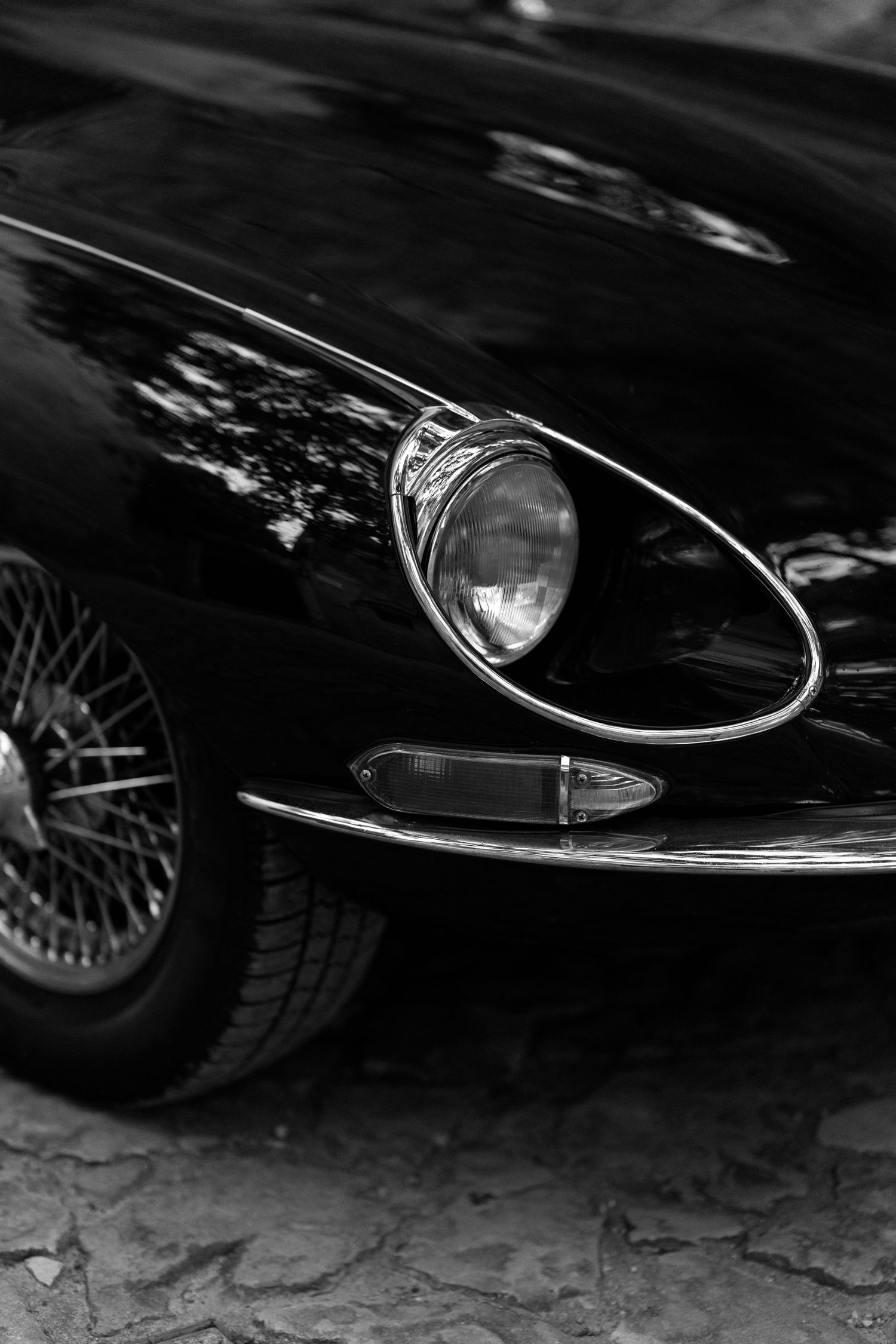 Close-up black and white photo showing the sleek front end details of a classic car with chrome trim and headlights.