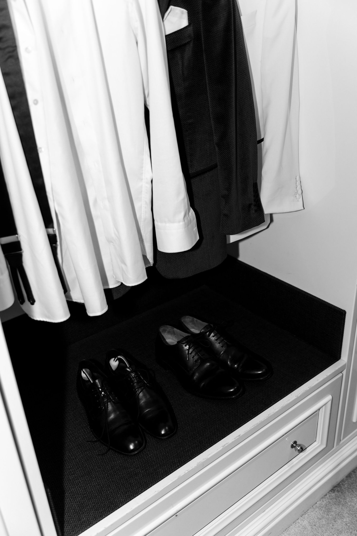 Black and white closet interior with hanging dress shirts and dress shoes placed neatly on the closet floor.