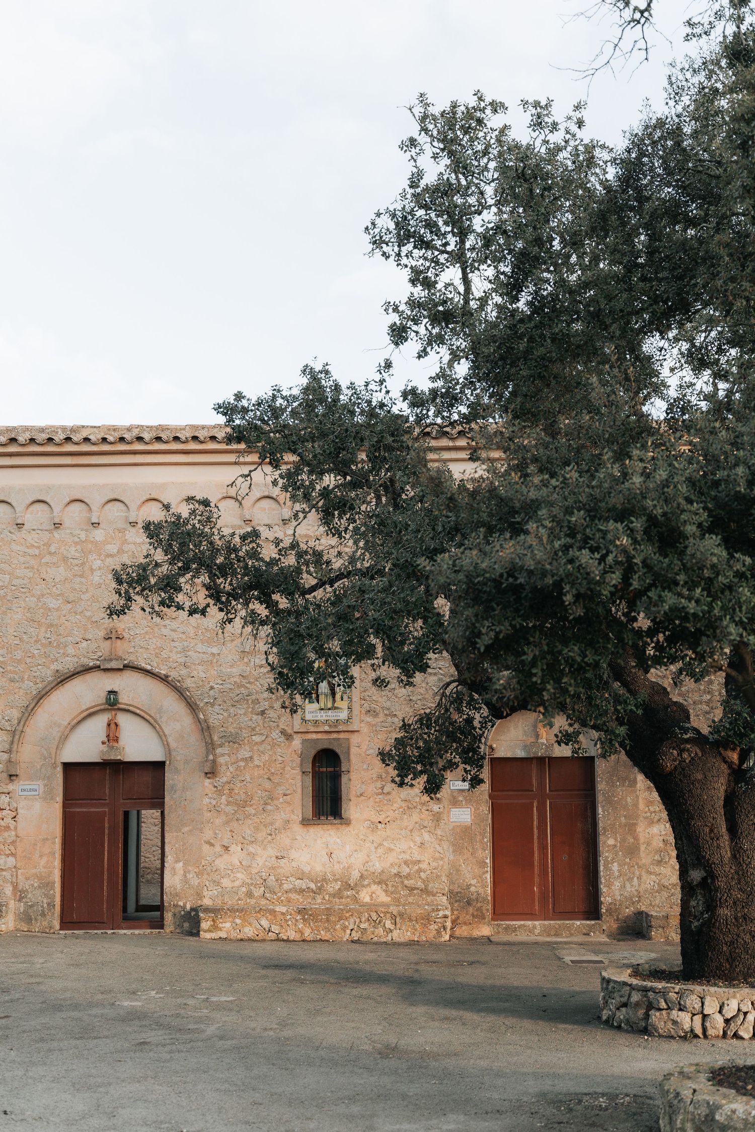 Stone courtyard with rustic wooden doors and arched entryways surrounded by olive trees.