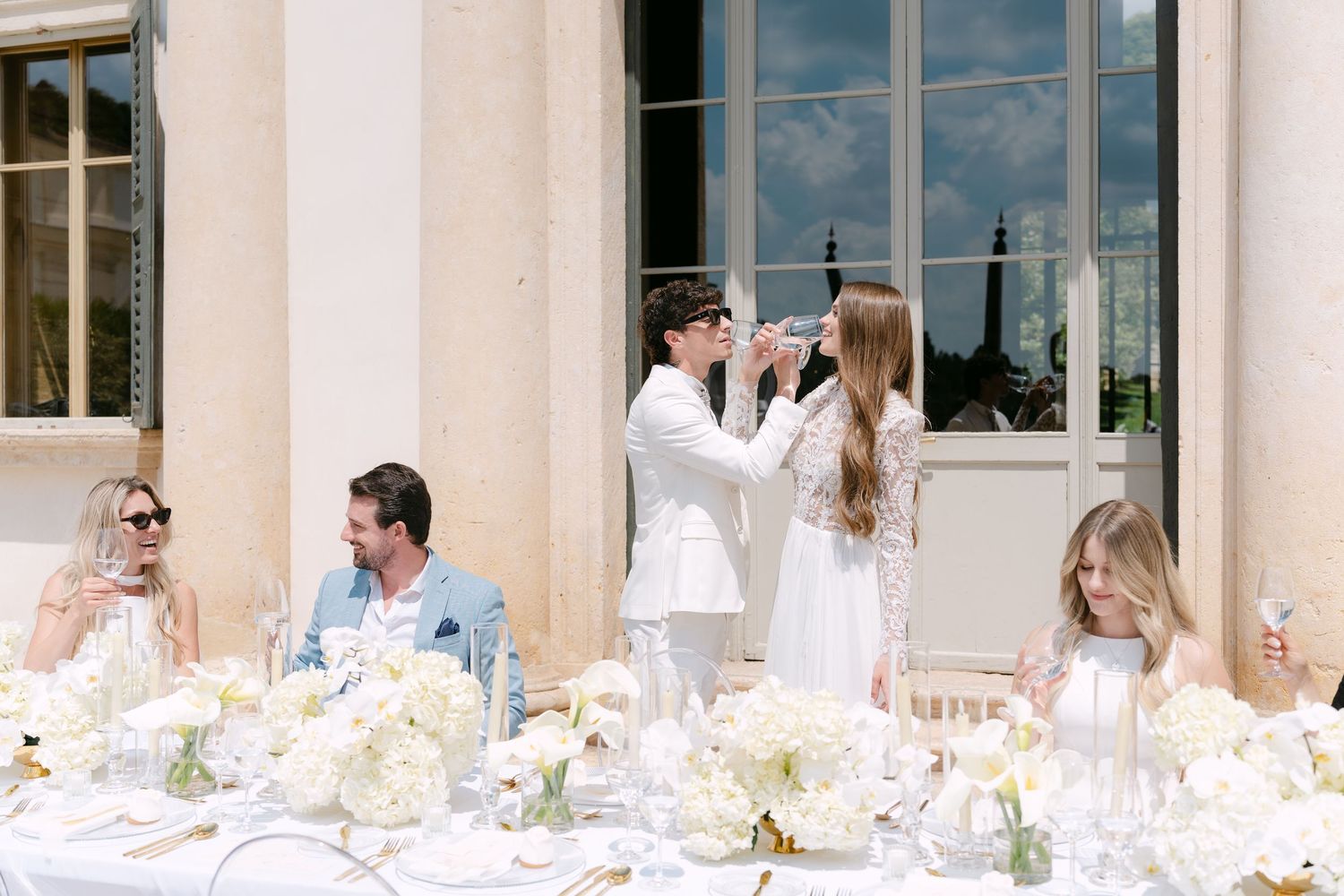A long table set for an elegant outdoor wedding reception with white linens and floral centerpieces along a columned terrace. Villa Mosconi