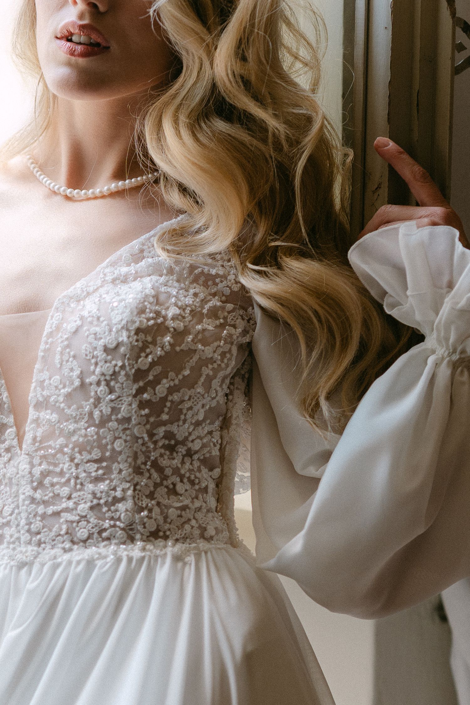 A white lace and chiffon dress with bishop sleeves and pearl necklace shown in a romantic vintage style portrait. Wedding Verona