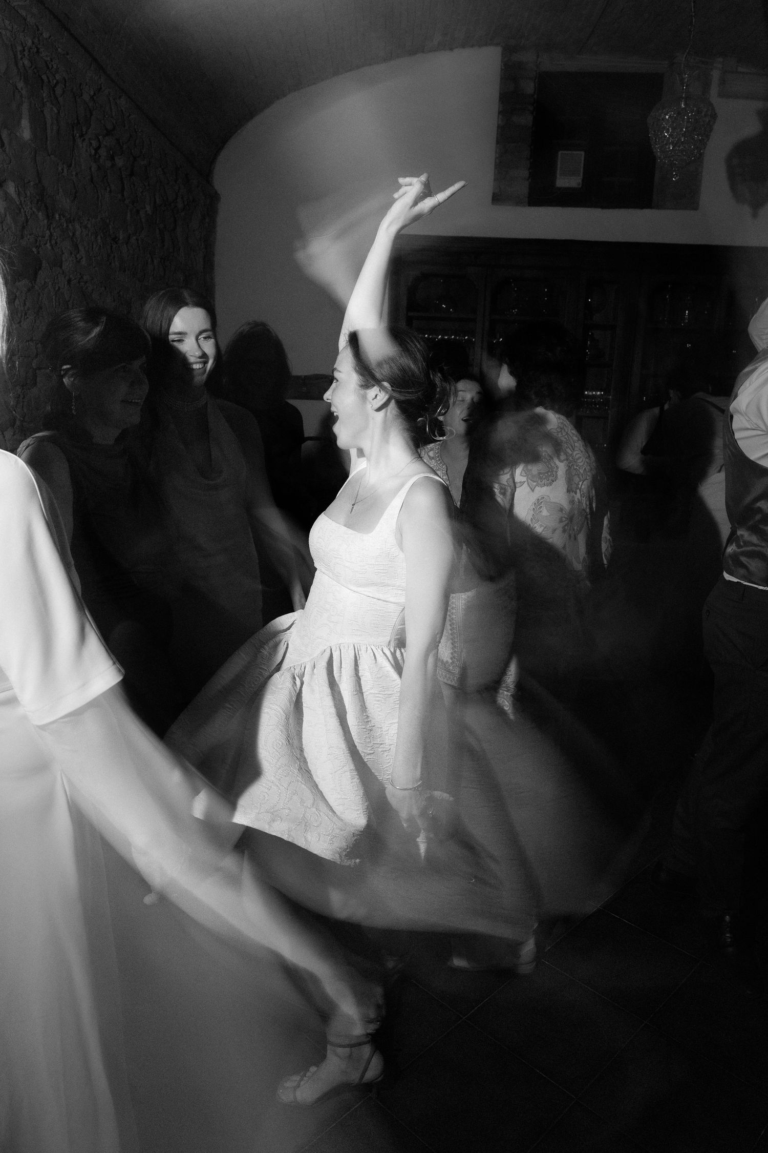 Black and white photo of a bride dancing joyfully at her wedding reception, arm raised, white dress swirling.