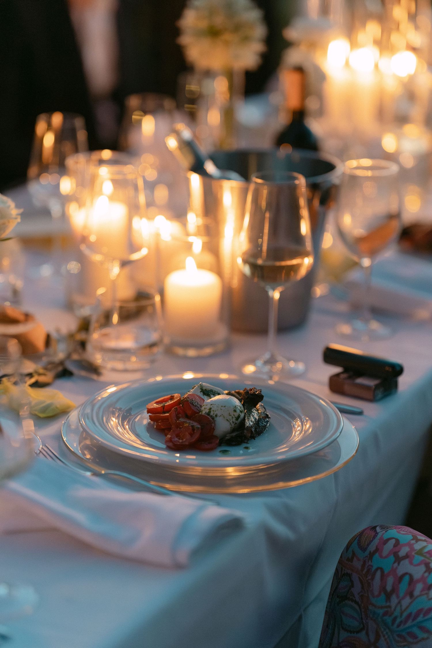 Elegant candlelit dinner table setting with glowing candles, crystal wine glasses, and a gourmet plated dish on white linen.