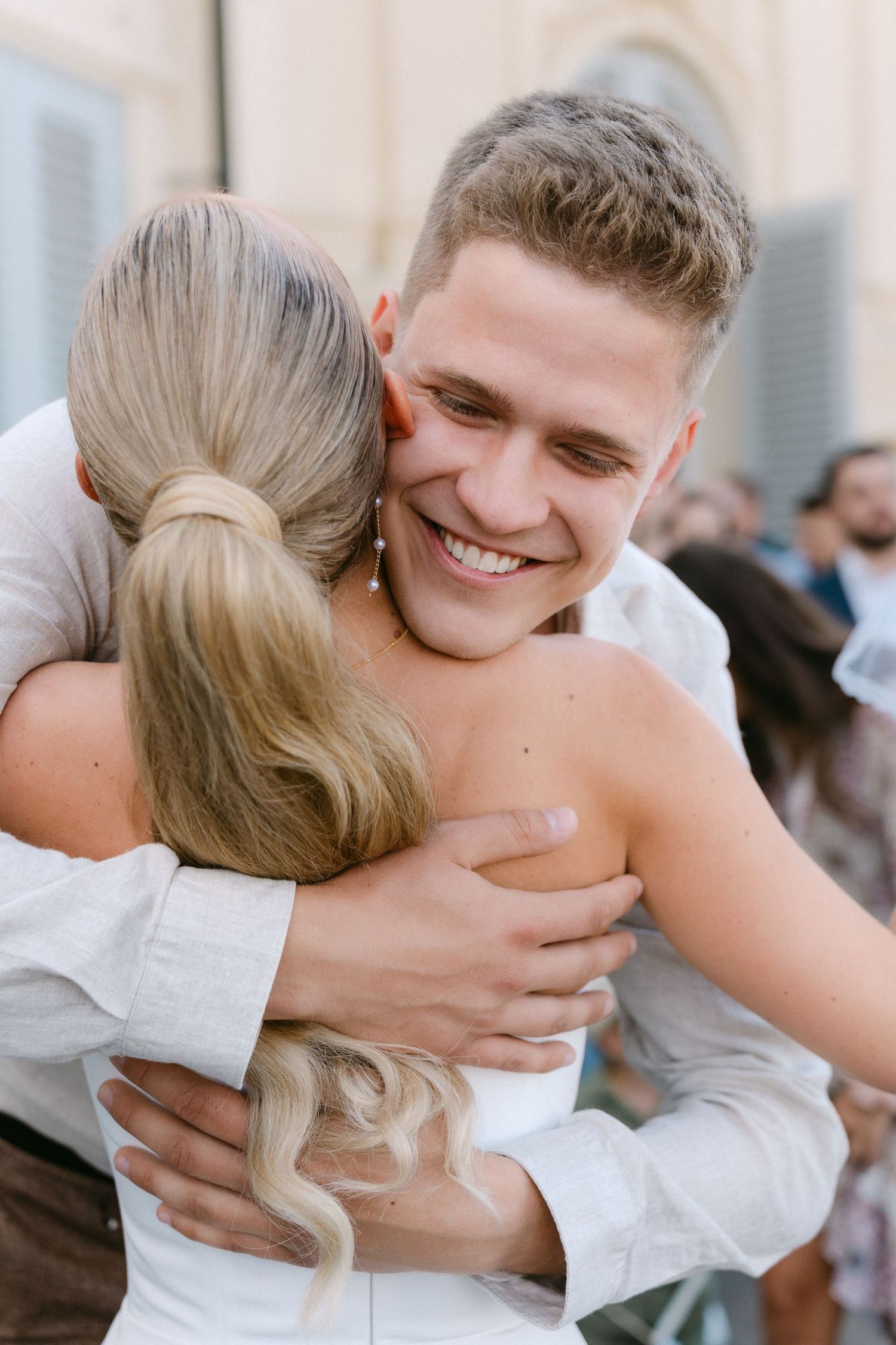 A joyful embrace between two people wearing white clothing at an outdoor celebration. Schloss Solitude