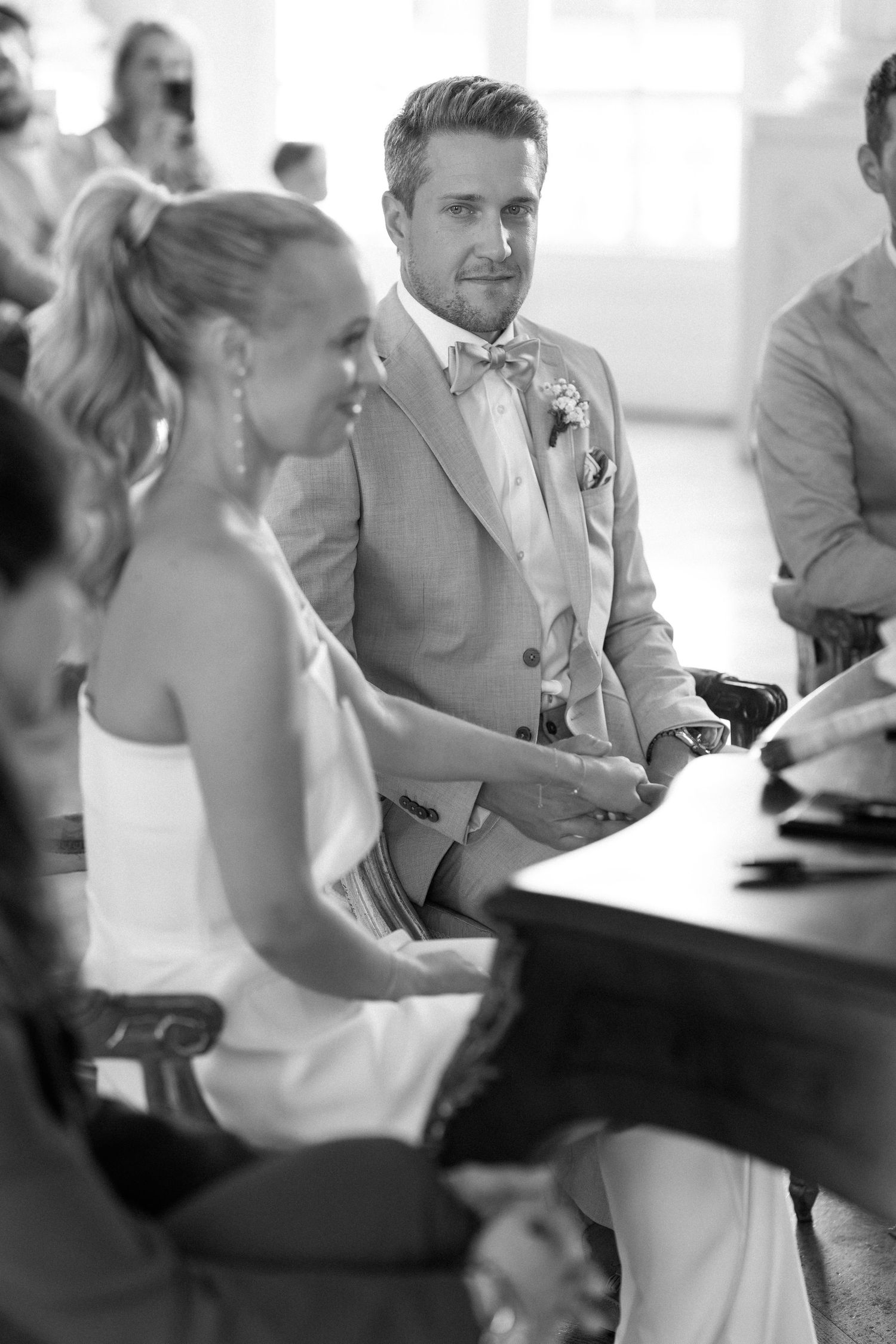 A black and white candid shot of wedding guests seated at tables during a reception celebration. Schloss Solitude