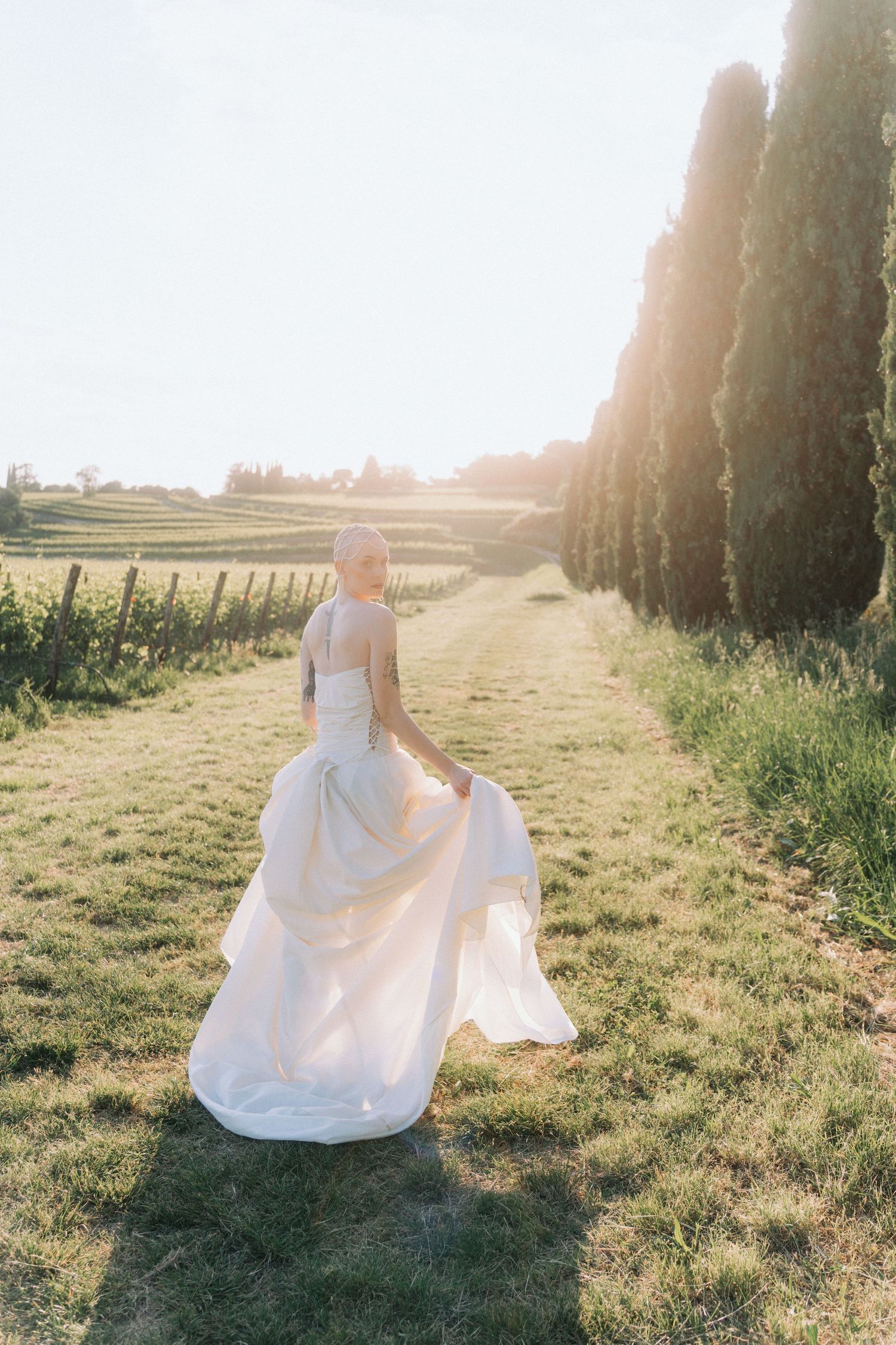 A person in a flowing white wedding dress sits gracefully in a sunlit field at golden hour.
