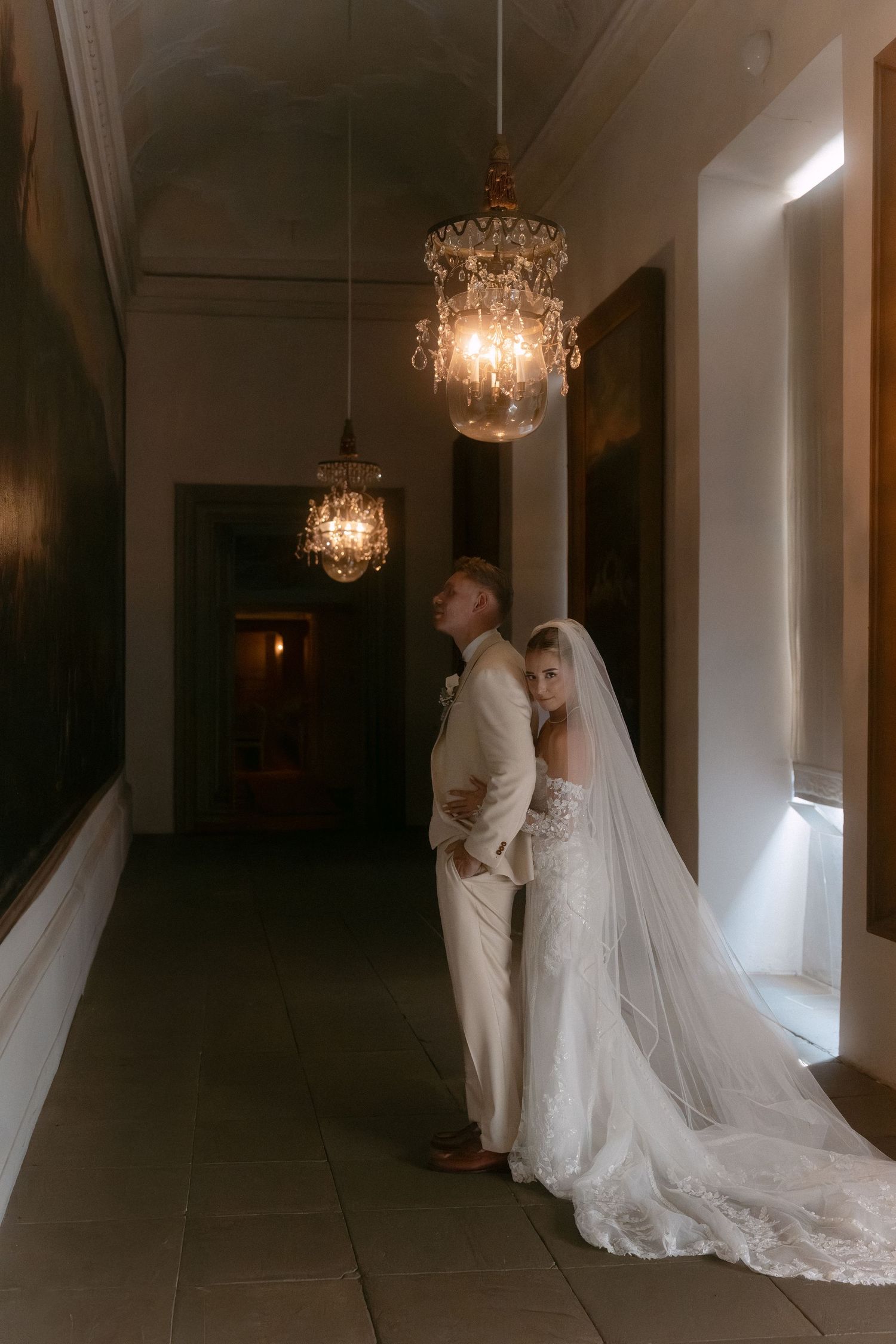 A romantic wedding couple shares an intimate moment in a dimly lit hallway beneath elegant crystal chandeliers. Schloss Ludwigsburg