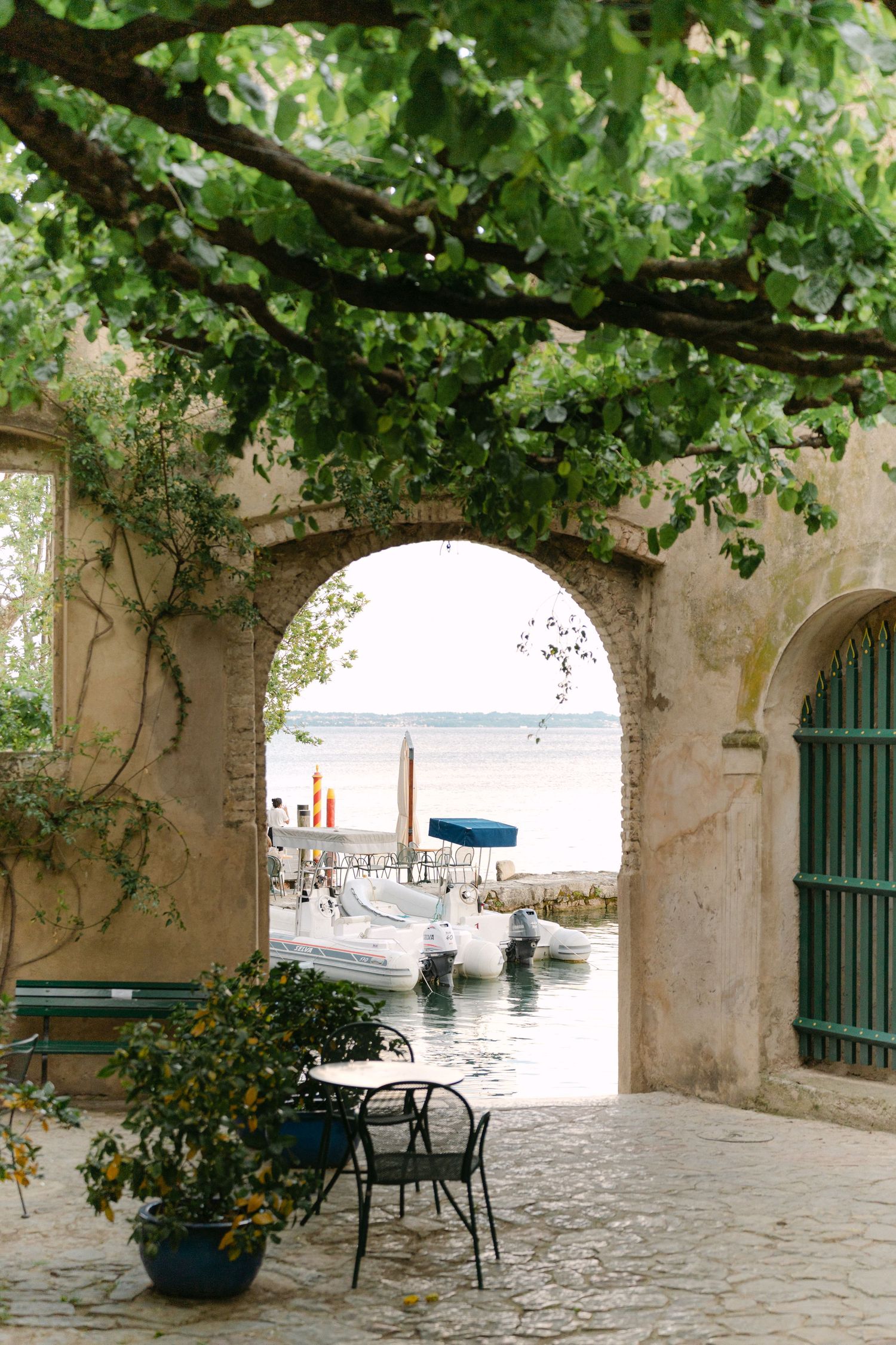 Charming archway in Mediterranean coastal town reveals harbor view with boats and turquoise water through stone passage.