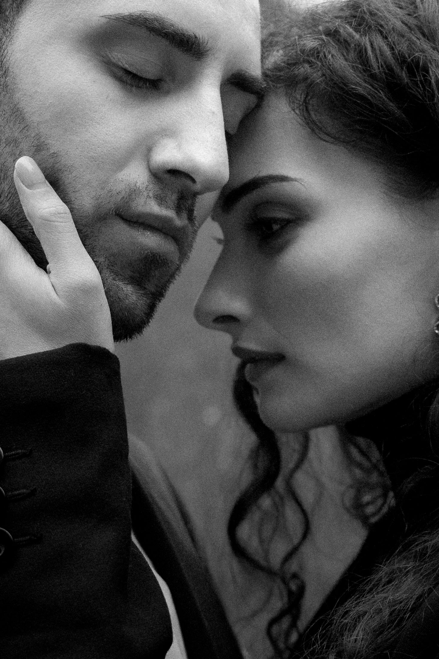A black and white intimate portrait of a couple in a tender moment with their faces close together.