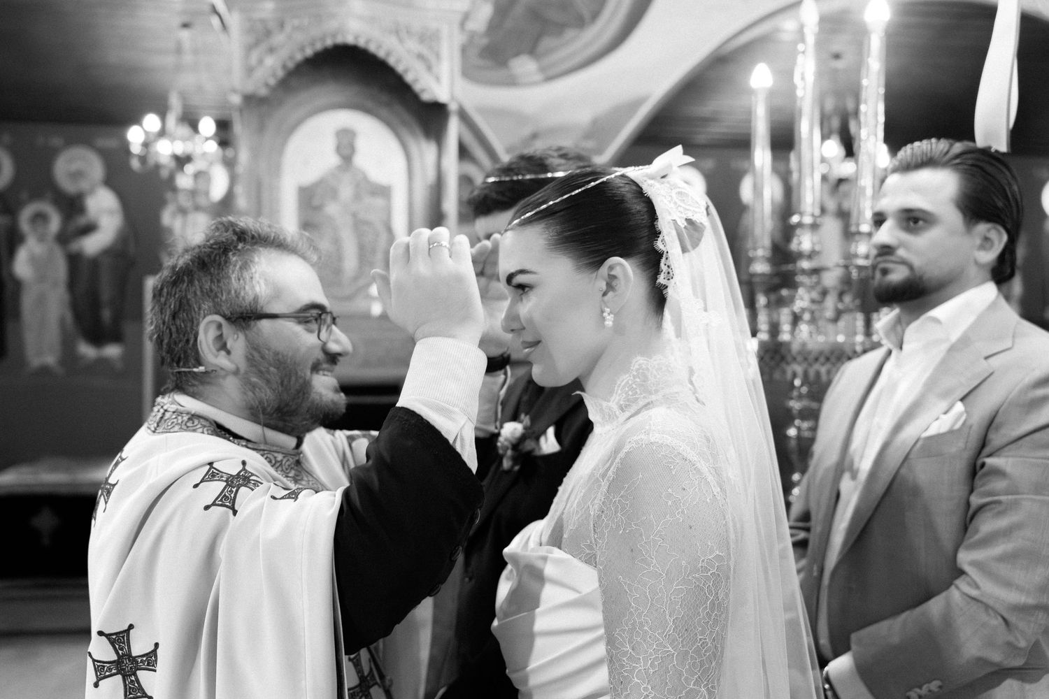 Priest blessing bride during Orthodox wedding ceremony in black and white photo.
