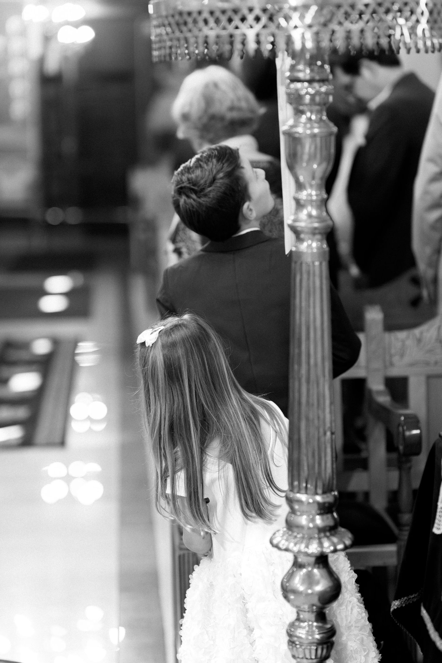 Black and white photo of a young girl in white dress standing beside a man in a church during a wedding ceremony.