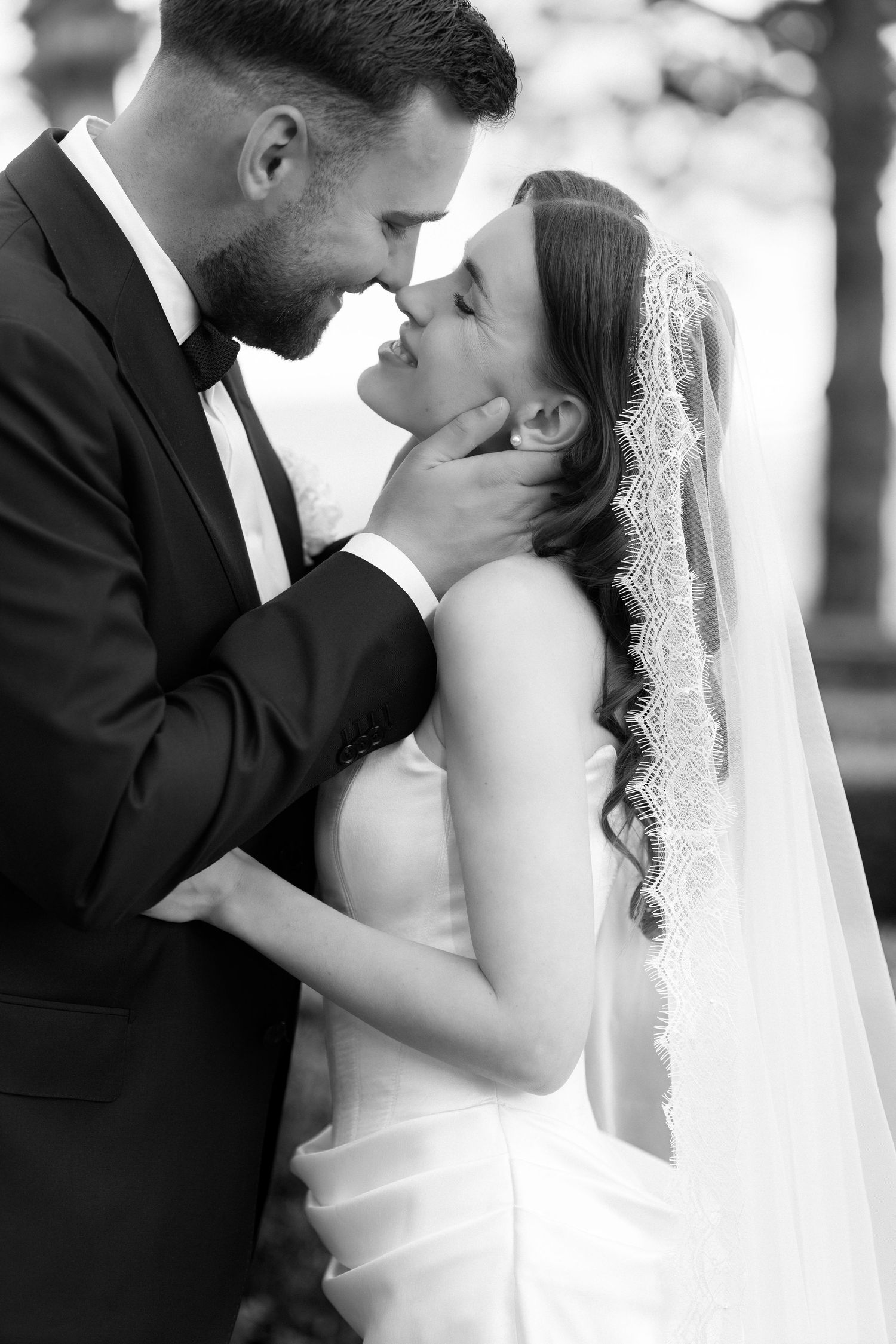 Black and white photo of a groom tenderly holding brides face as they share an intimate moment in wedding attire.