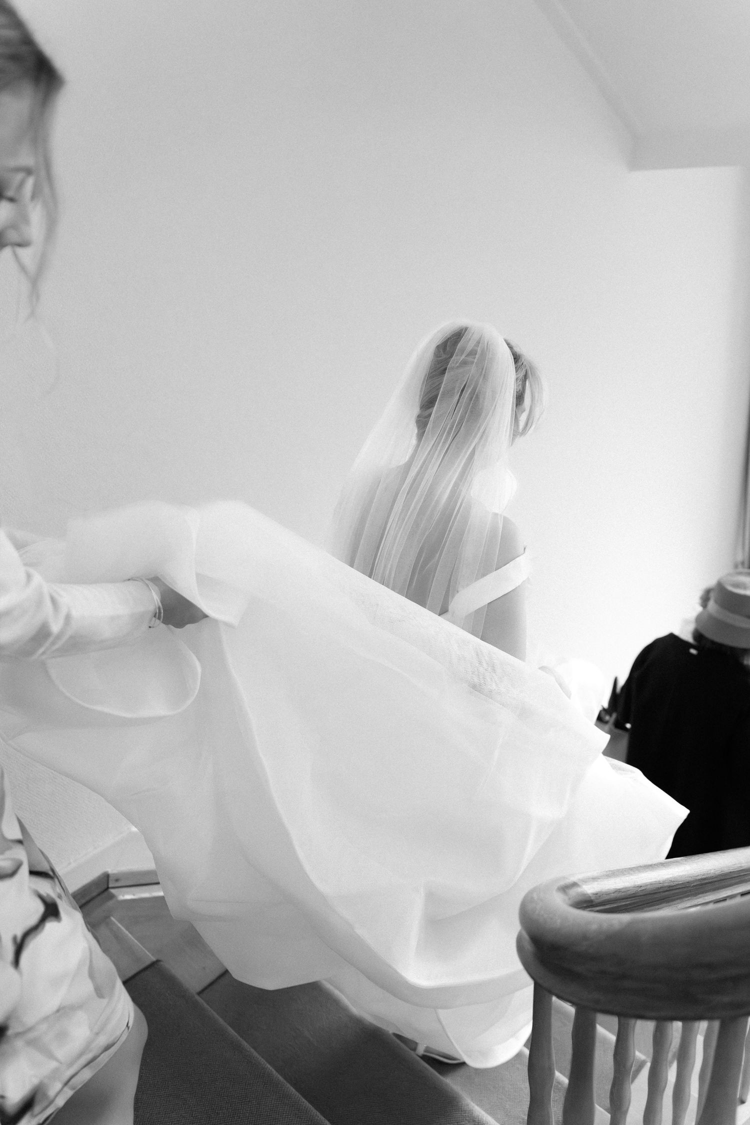 Black and white image of a bride's flowing white wedding dress being adjusted in a getting ready moment.