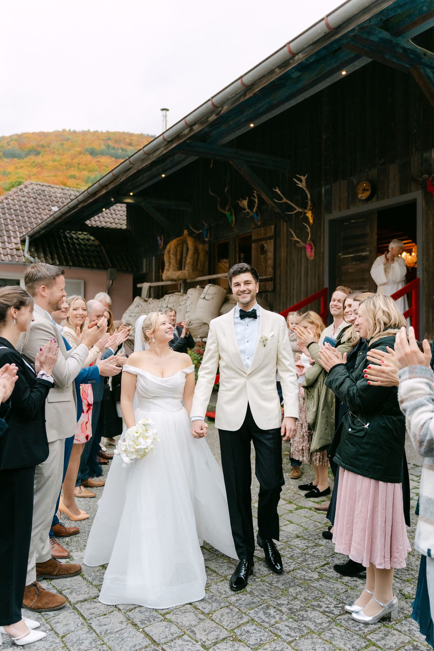 Wedding celebration at rustic venue with guests lining pathway to throw confetti as newlyweds walk through.
