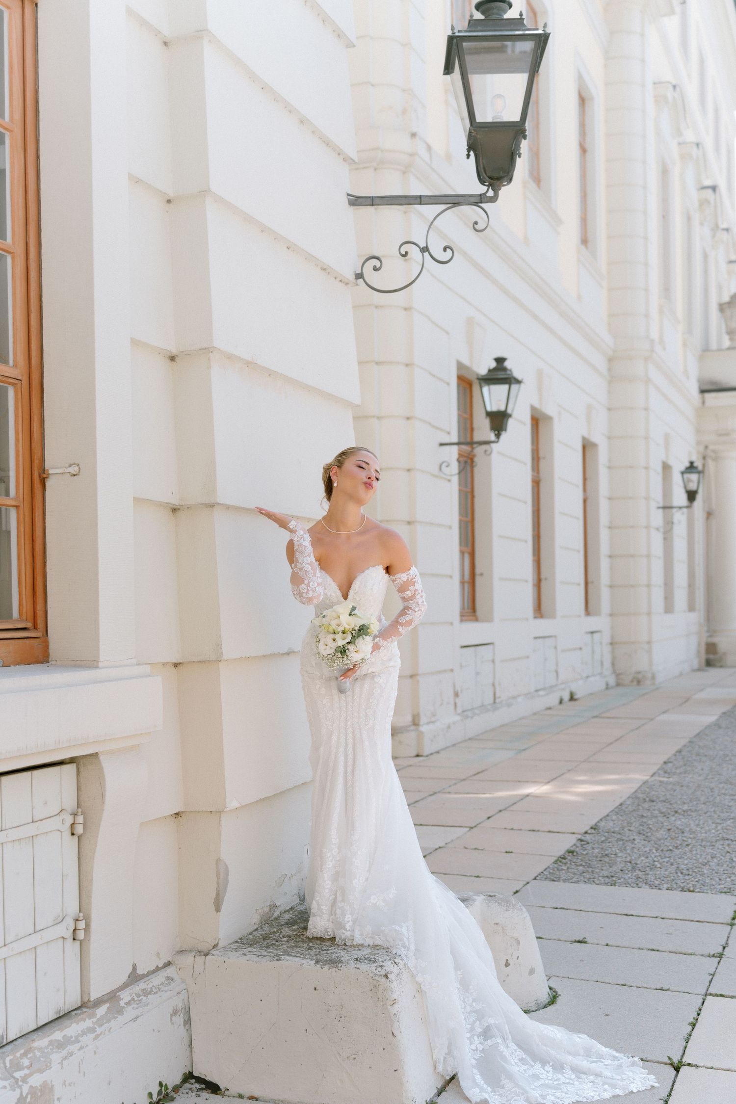 Elegant bride in white lace gown poses gracefully along a bright colonnade walkway with classic architecture. Schloss Ludwigsburg