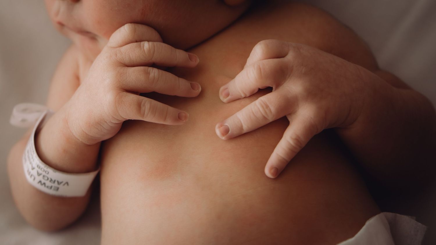 Close-up of gentle hands caressing baby's delicate skin in soft lighting.
