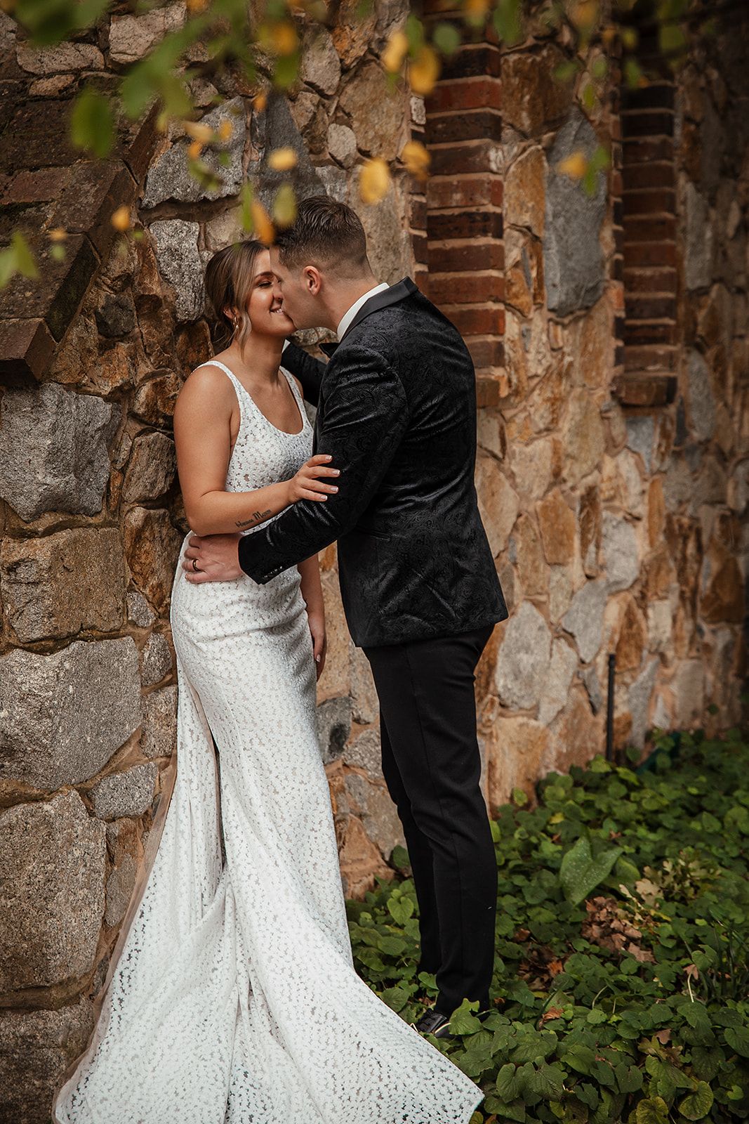 Couple shares intimate moment against rustic brick wall with autumn foliage.
Wedding photography