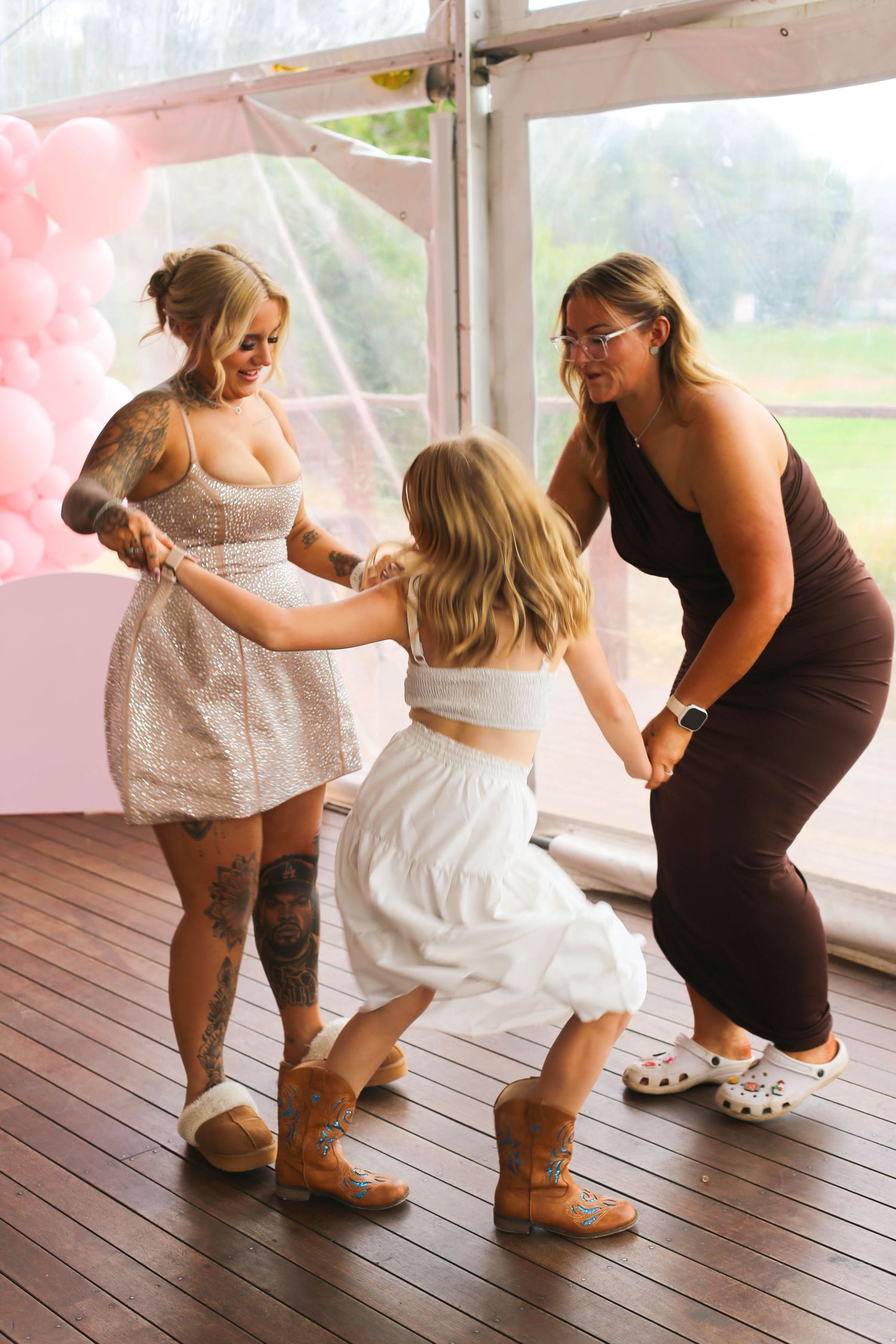 Dancing figures in formal attire showing playful moves on a wooden deck with pink balloon decor.