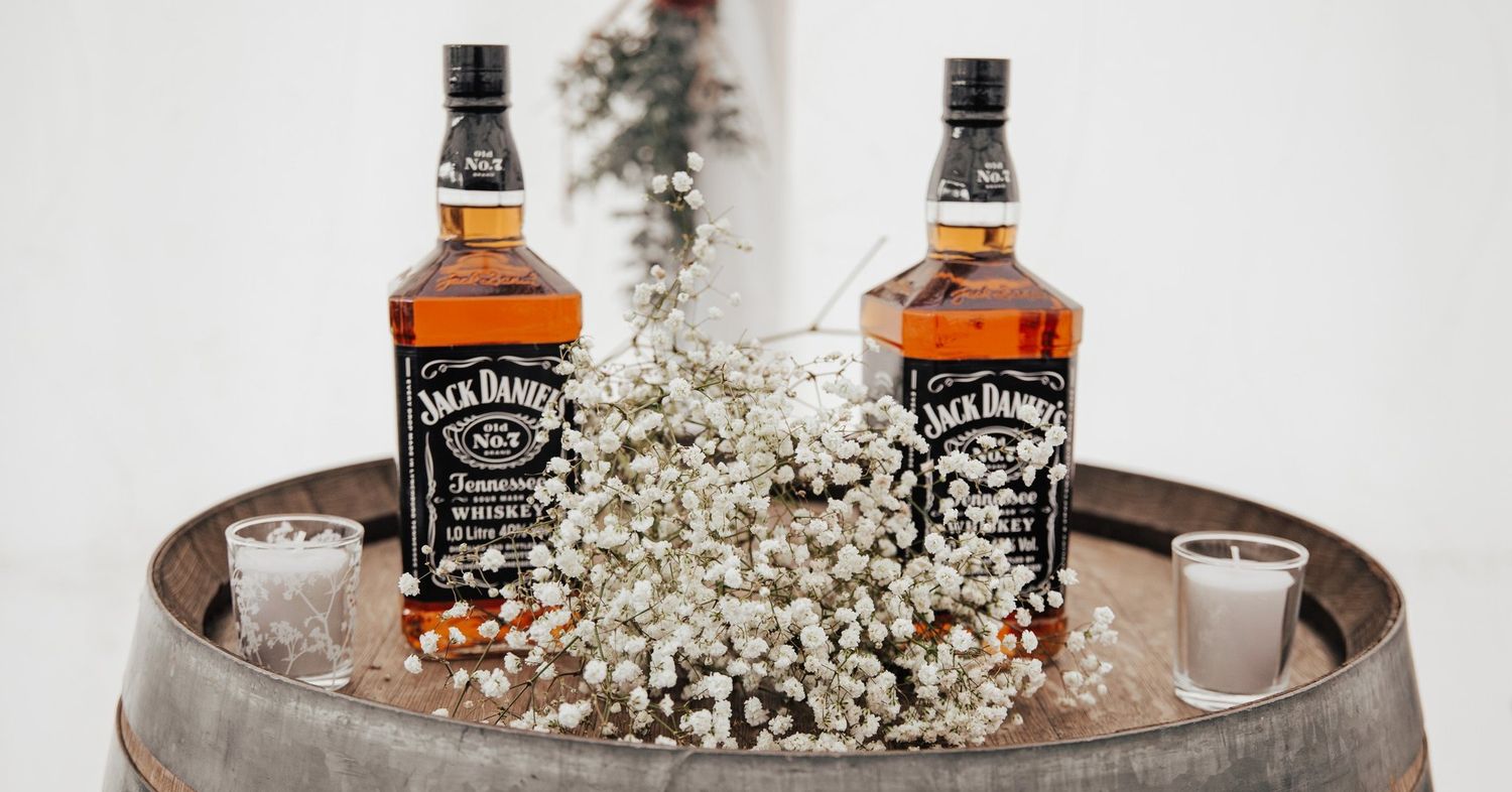 Jack Daniel's whiskey bottles displayed with baby's breath flowers on rustic tray.