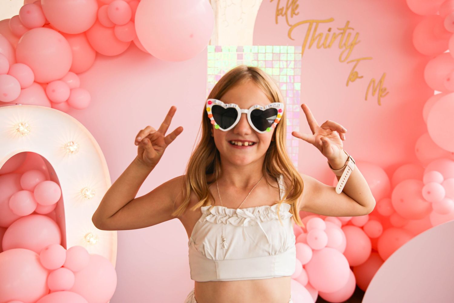 Fun poses and peace signs against a pink balloon wall backdrop.